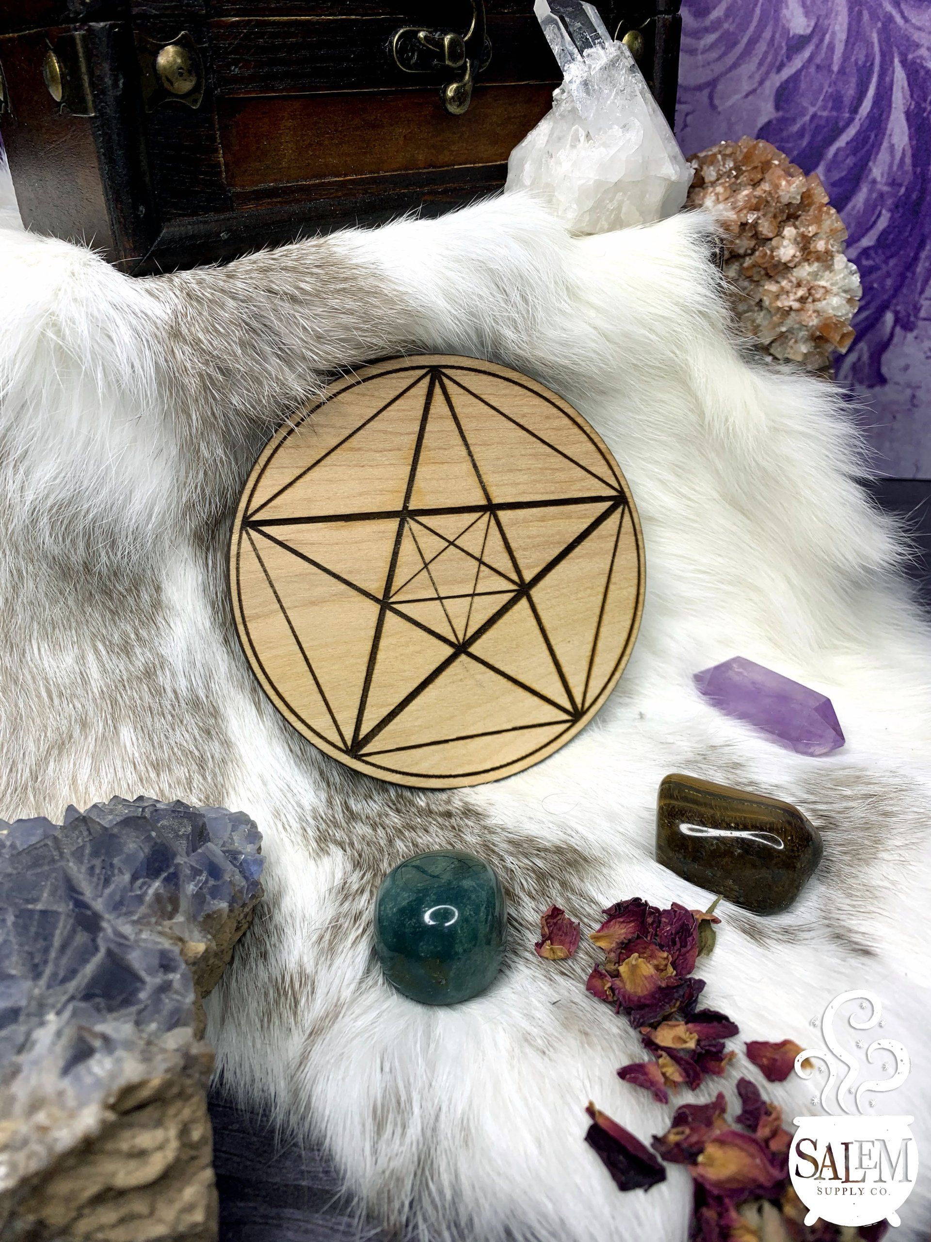 A wooden pentagram is sitting on top of a fur blanket surrounded by crystals.