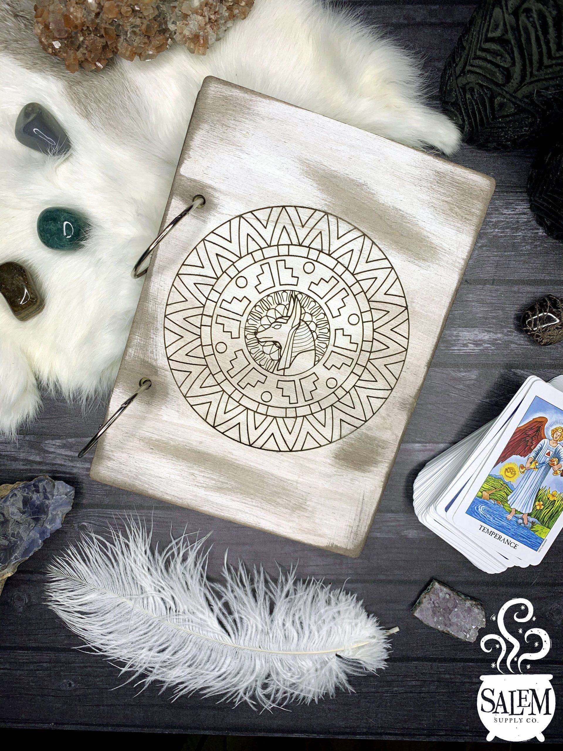 A book is sitting on a wooden table next to a feather and tarot cards.