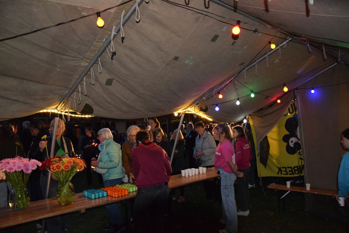 Mensen onder een tent op een avondmarkt met lichtslingers en kleurrijke kraampjes.