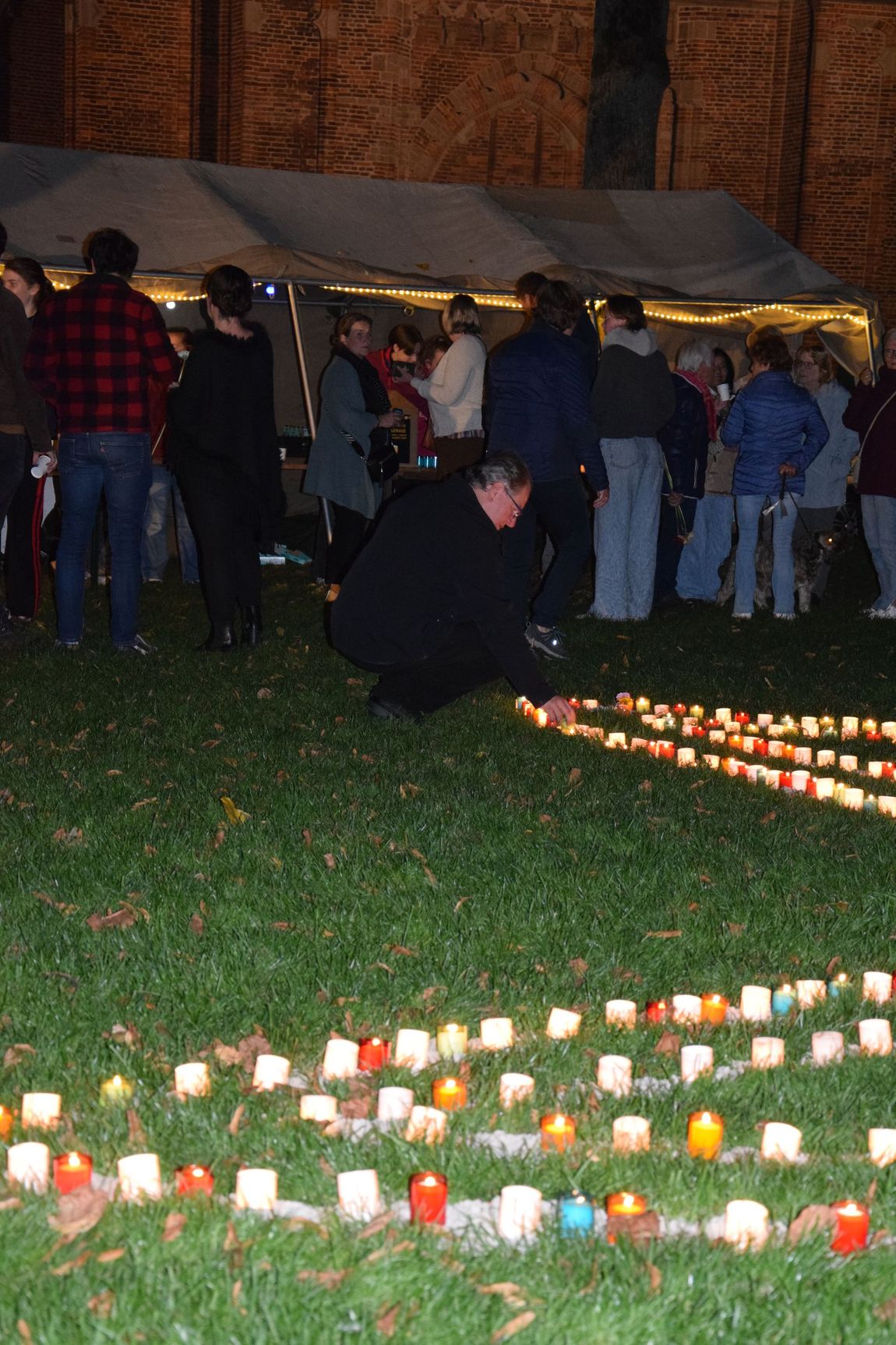 Mensen verzamelden zich 's avonds voor een kaarsverlichte wake op een grasveld, vlakbij een tent.