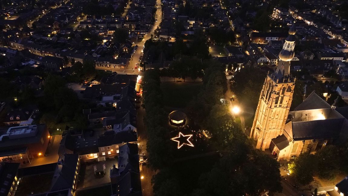Luchtfoto 's nachts van een verlicht stadsplein met een gloeiende stervormige lichtshow en hoge, verlichte gebouwen.