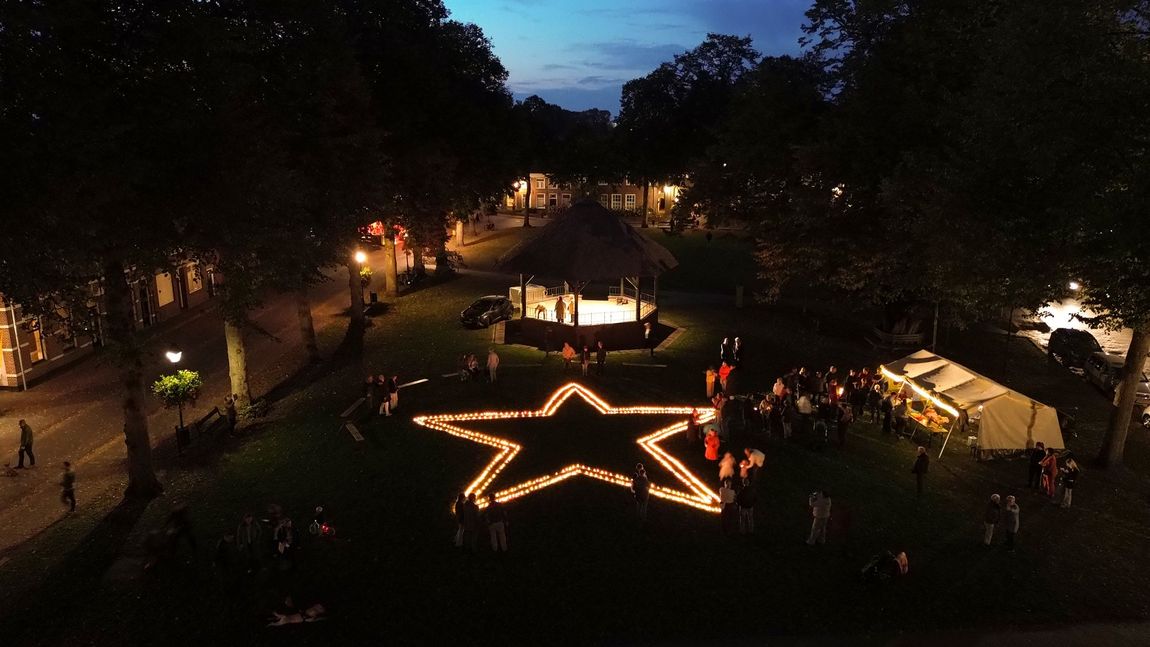 Een park 's nachts met een grote, verlichte sterrencontour en mensen eromheen verzameld.