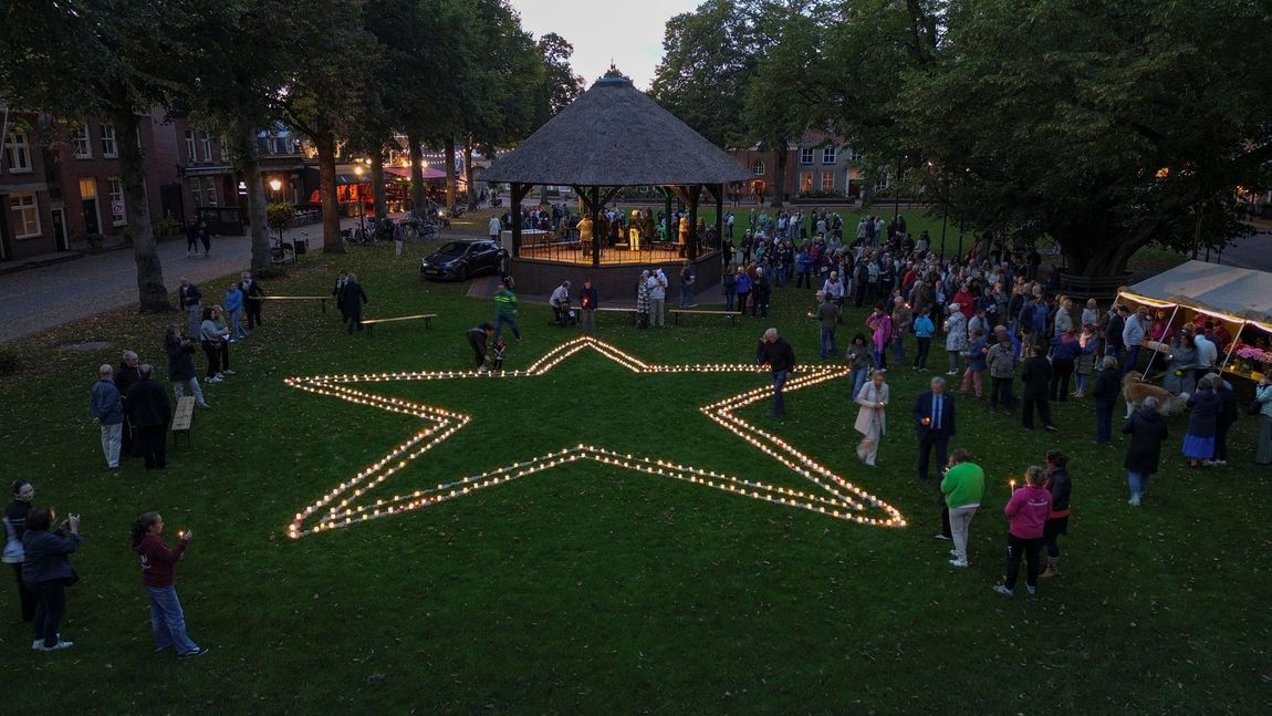 Een stervormige lichtshow in een park bij schemering, omringd door mensen in de buurt van een verlicht paviljoen.