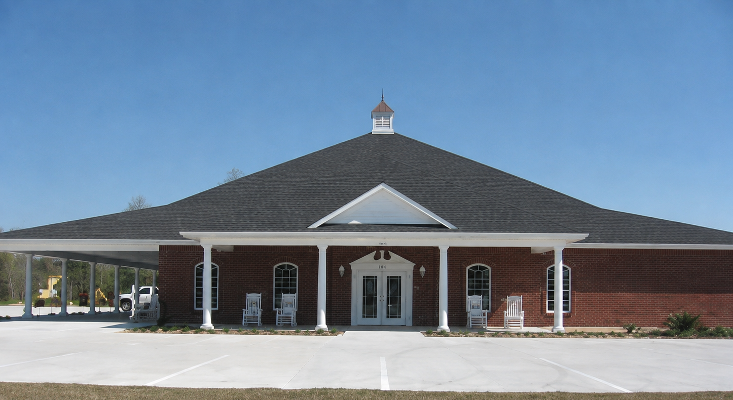 Single-story brick building with a dark shingled roof and white columns under a clear blue sky