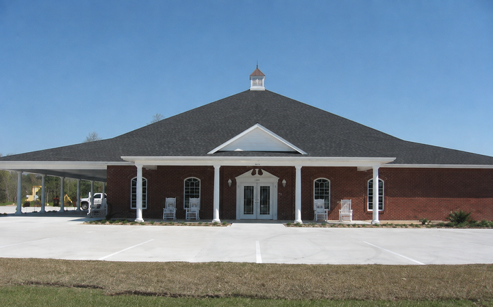 Brick building with a dark roof, white columns, and a central entrance under a clear blue sky