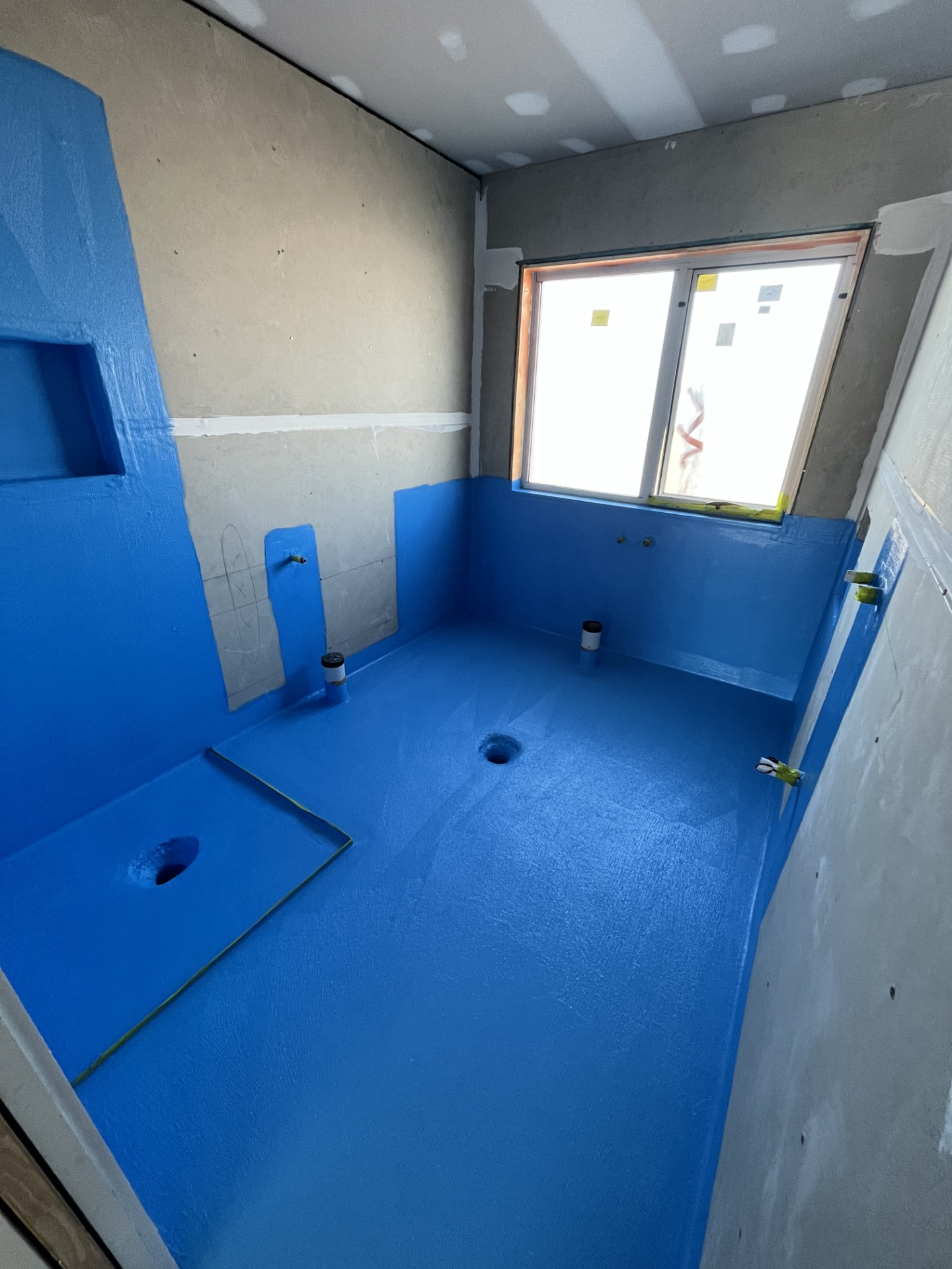 Blue-tiled bathroom with a window, shower fixtures, and unfinished walls under renovation