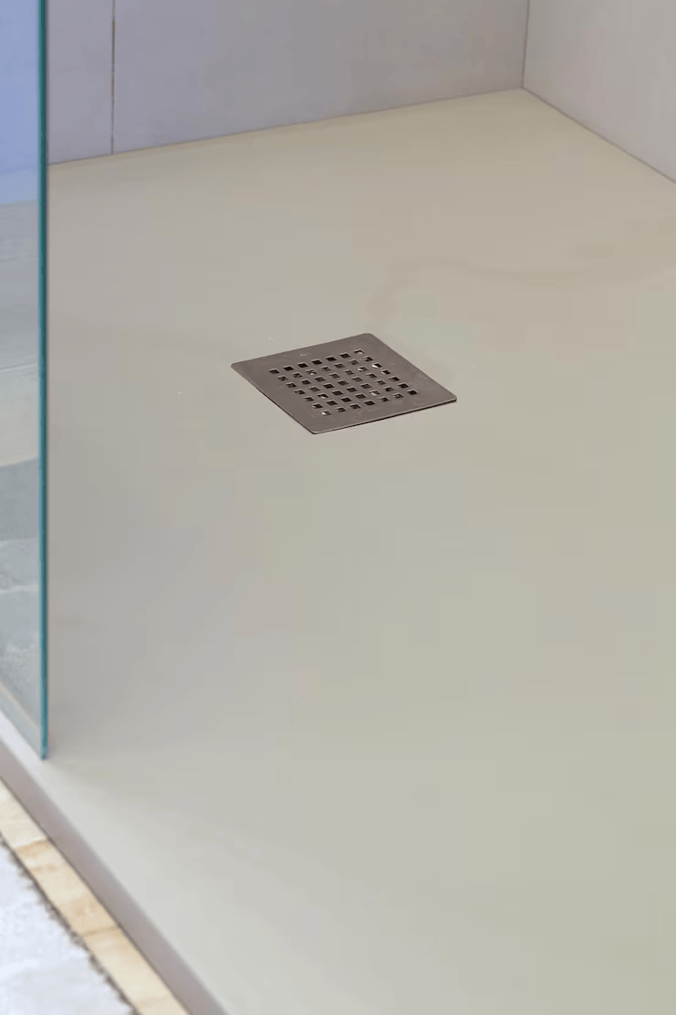 A beige, low-profile shower floor with a centered, square stainless steel drain grate, viewed from an angle.