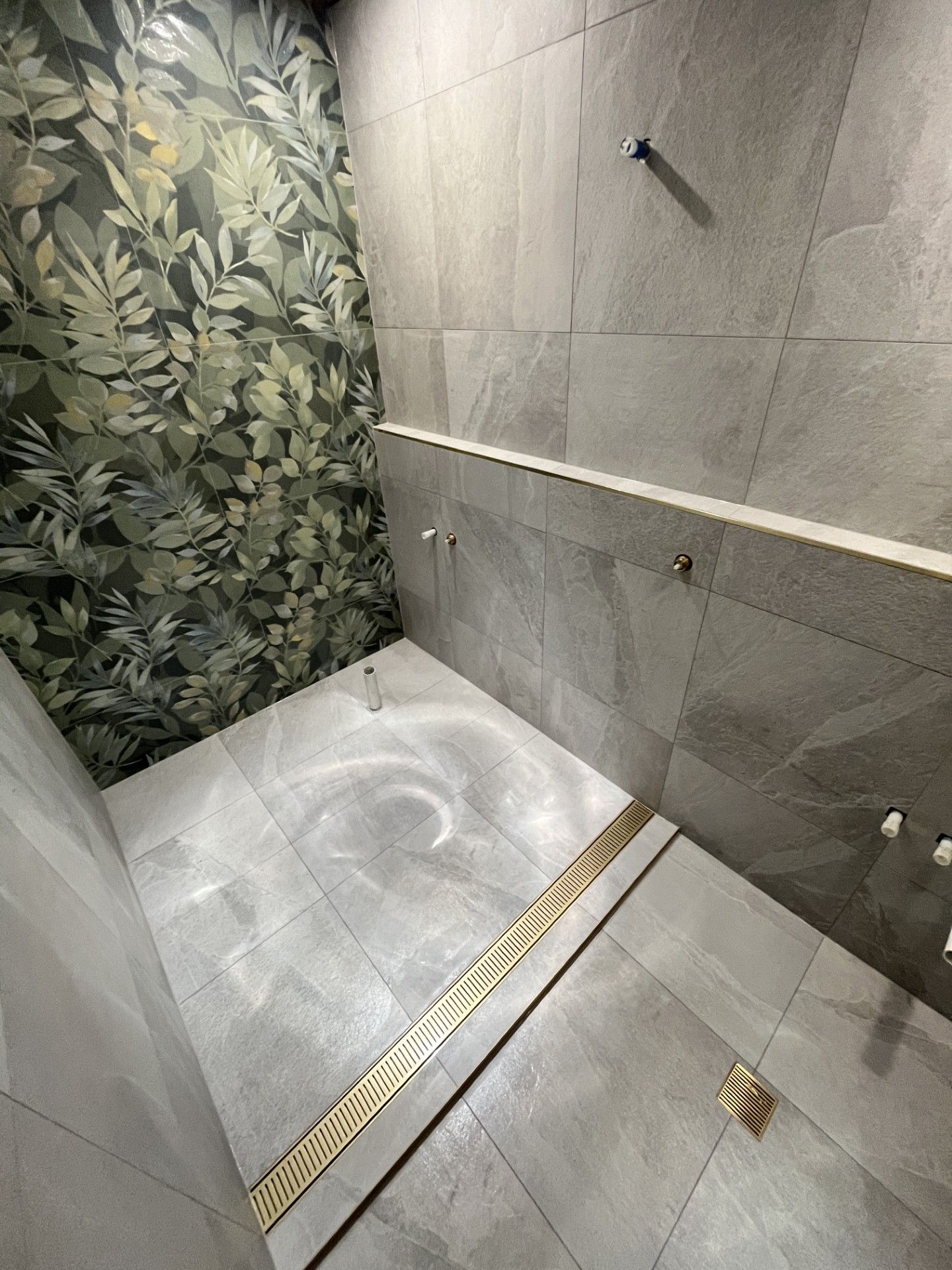 Small tiled walk-in shower with floral accent wall, gray tiles, bench, and linear drain.