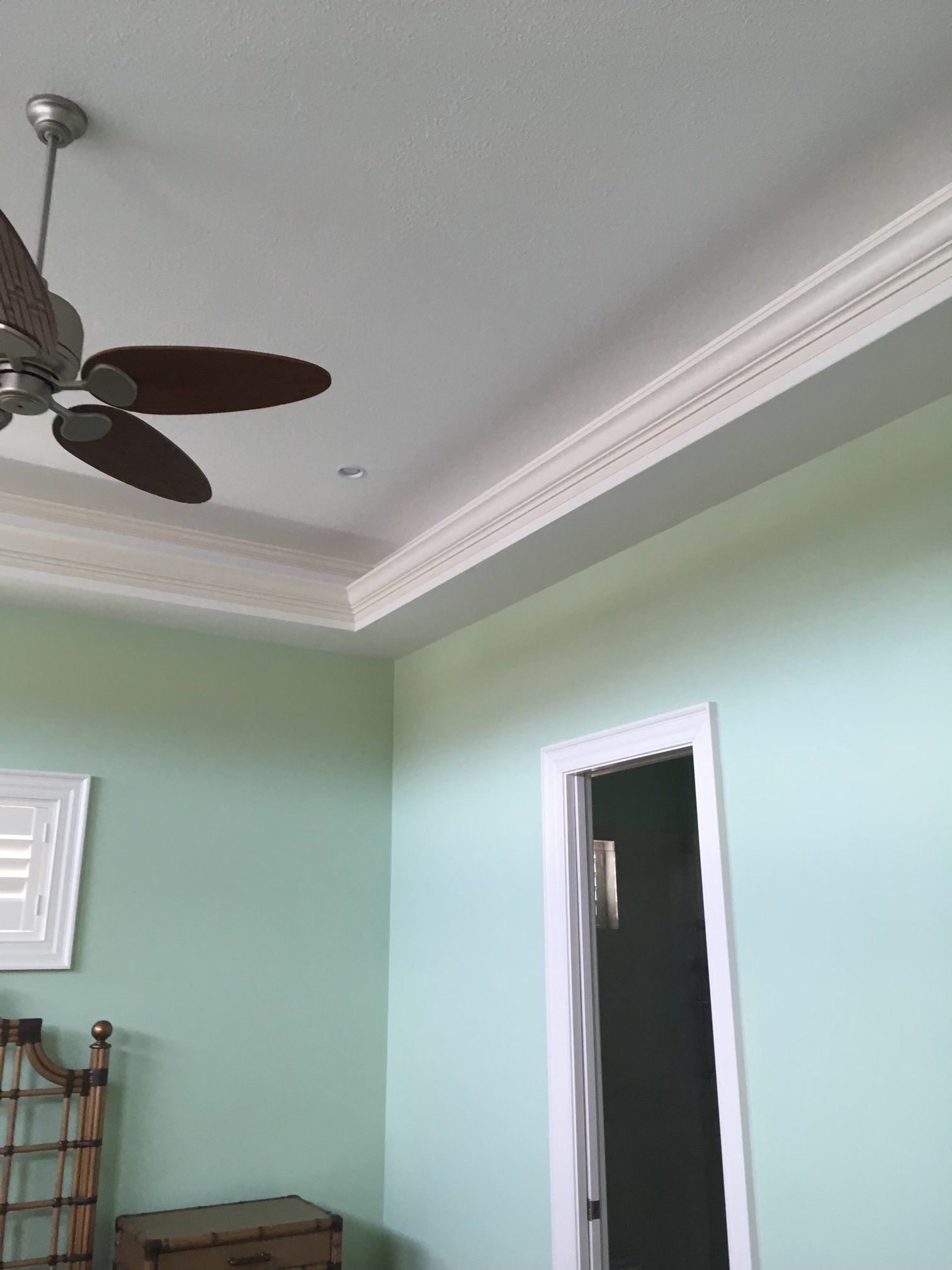 Mint-green bedroom with ceiling fan, white crown molding, and open doorway