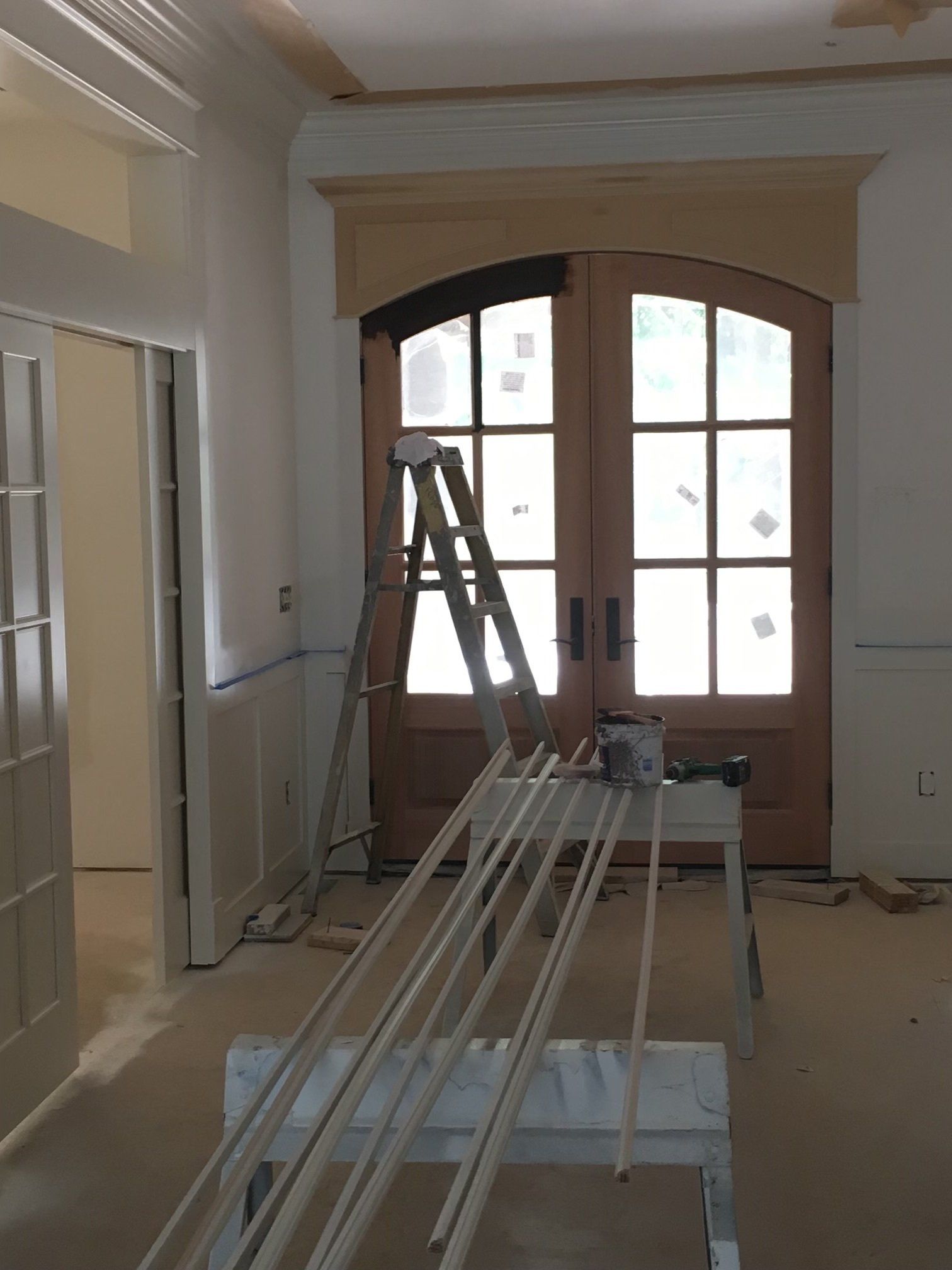 Indoor hallway with a ladder and building materials near a wooden double door, suggesting renovation work