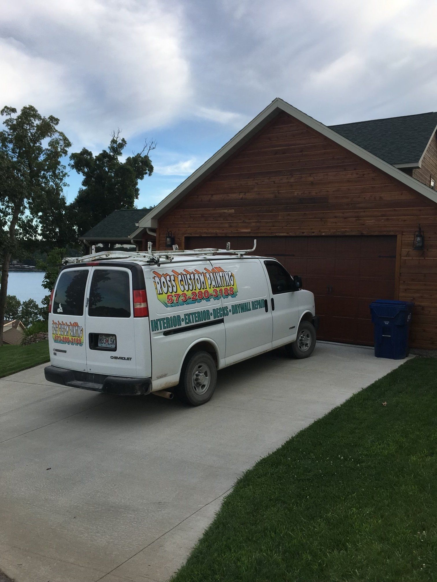 White van with a colorful logo parked in a driveway beside a brick house and garage.