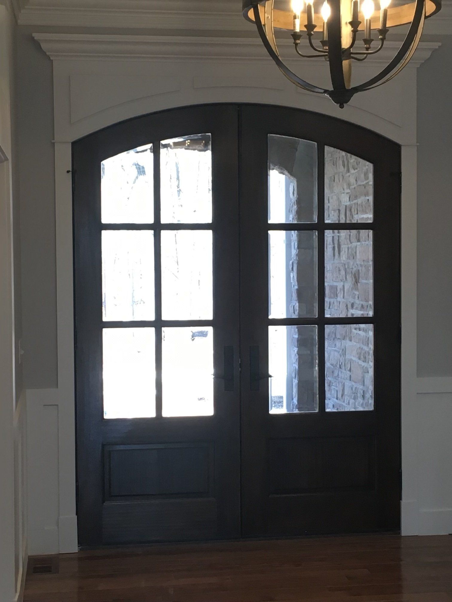 Dark double front doors with glass panes under a hanging chandelier in a home entryway