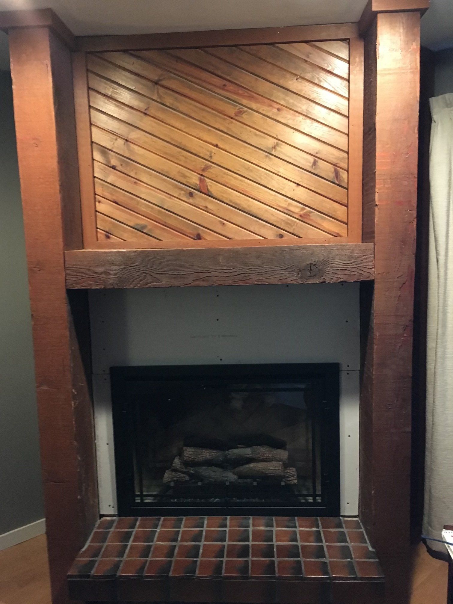 Built-in brick fireplace with dark mantel and diagonal wood paneling above