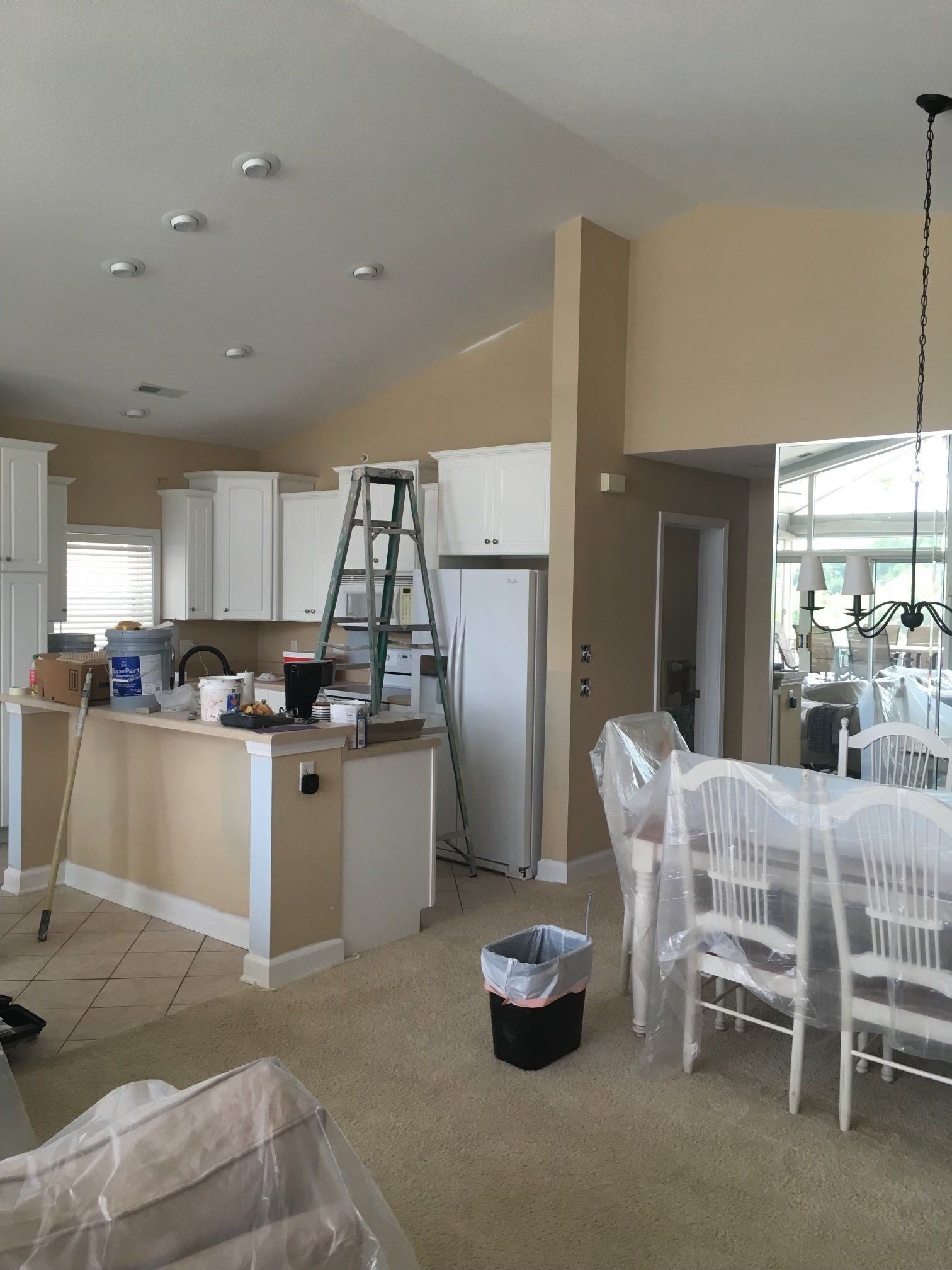 Kitchen and dining area with white cabinets, a ladder, and a dining table covered in plastic.