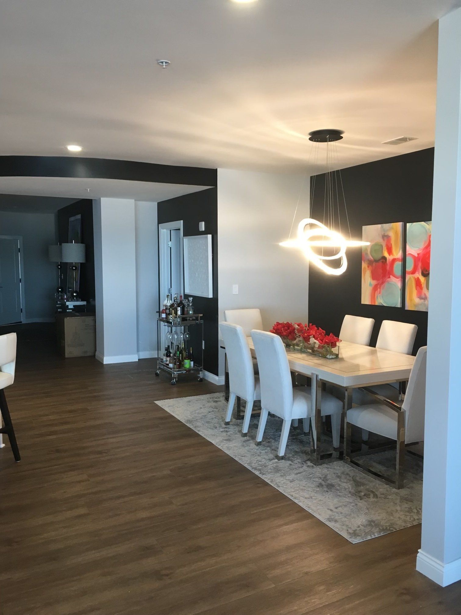 Modern dining room with white chairs, glass table, red flowers, and a glowing pendant light adjacent to an open living area
