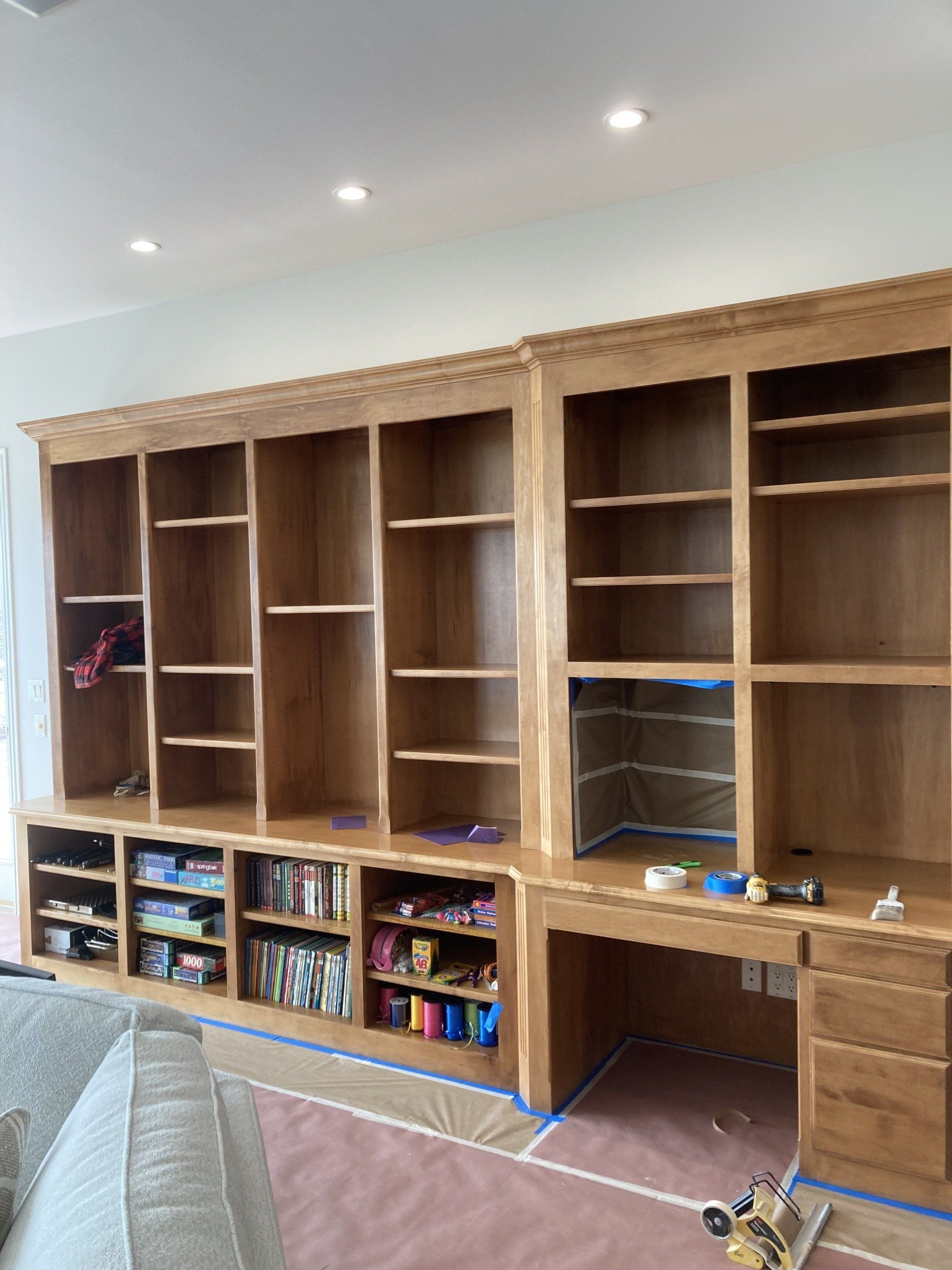 Built-in wooden wall cabinets with shelves and drawers in a living room, with toys and books below