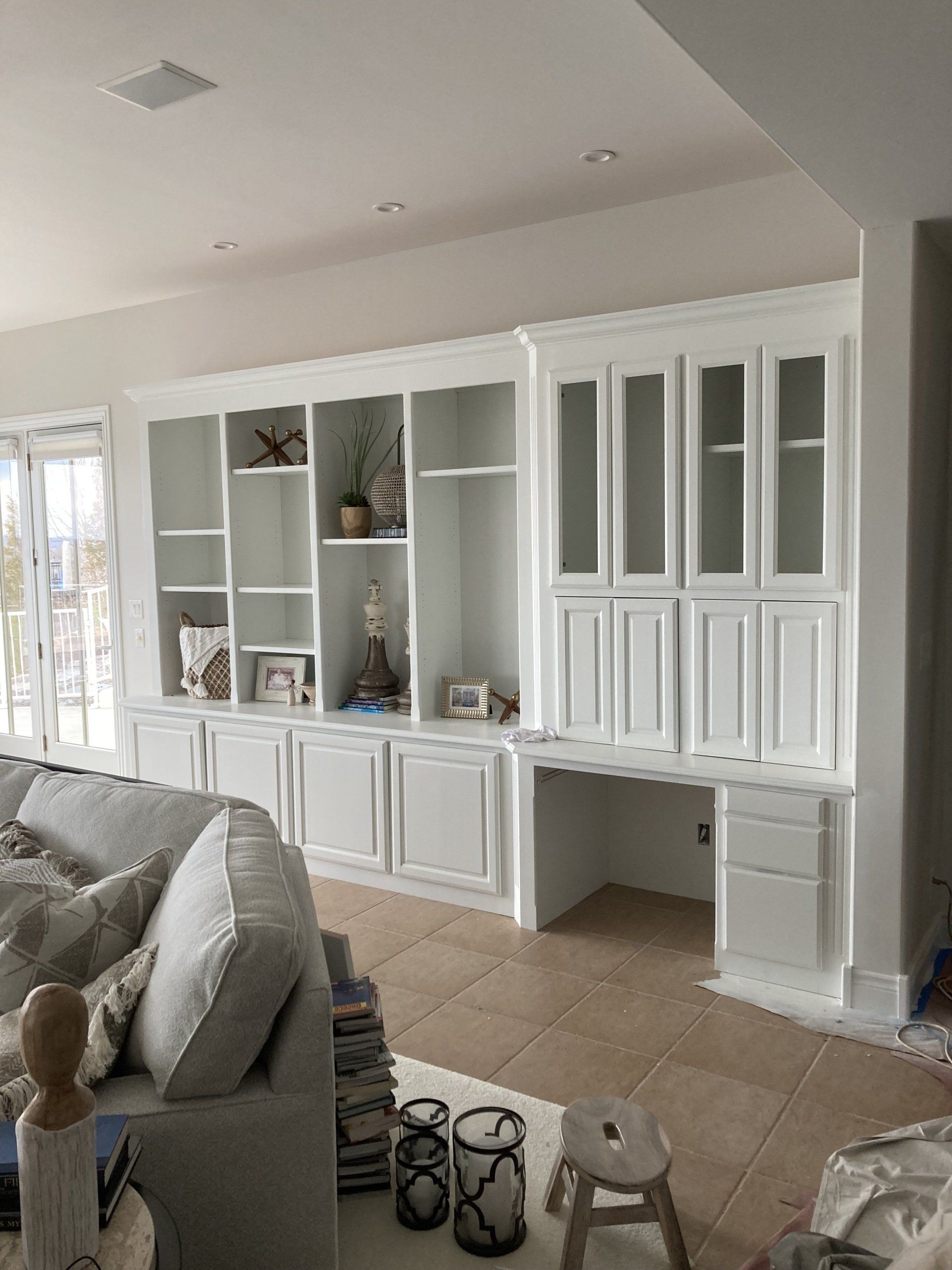 Living room with white built-in cabinets, display shelves, and a beige sectional sofa on tile floor.