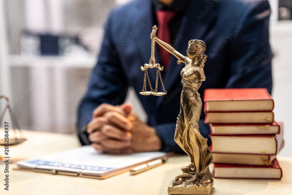 Lady Justice statue with balanced scales beside legal books and an attorney’s desk, symbolizing just