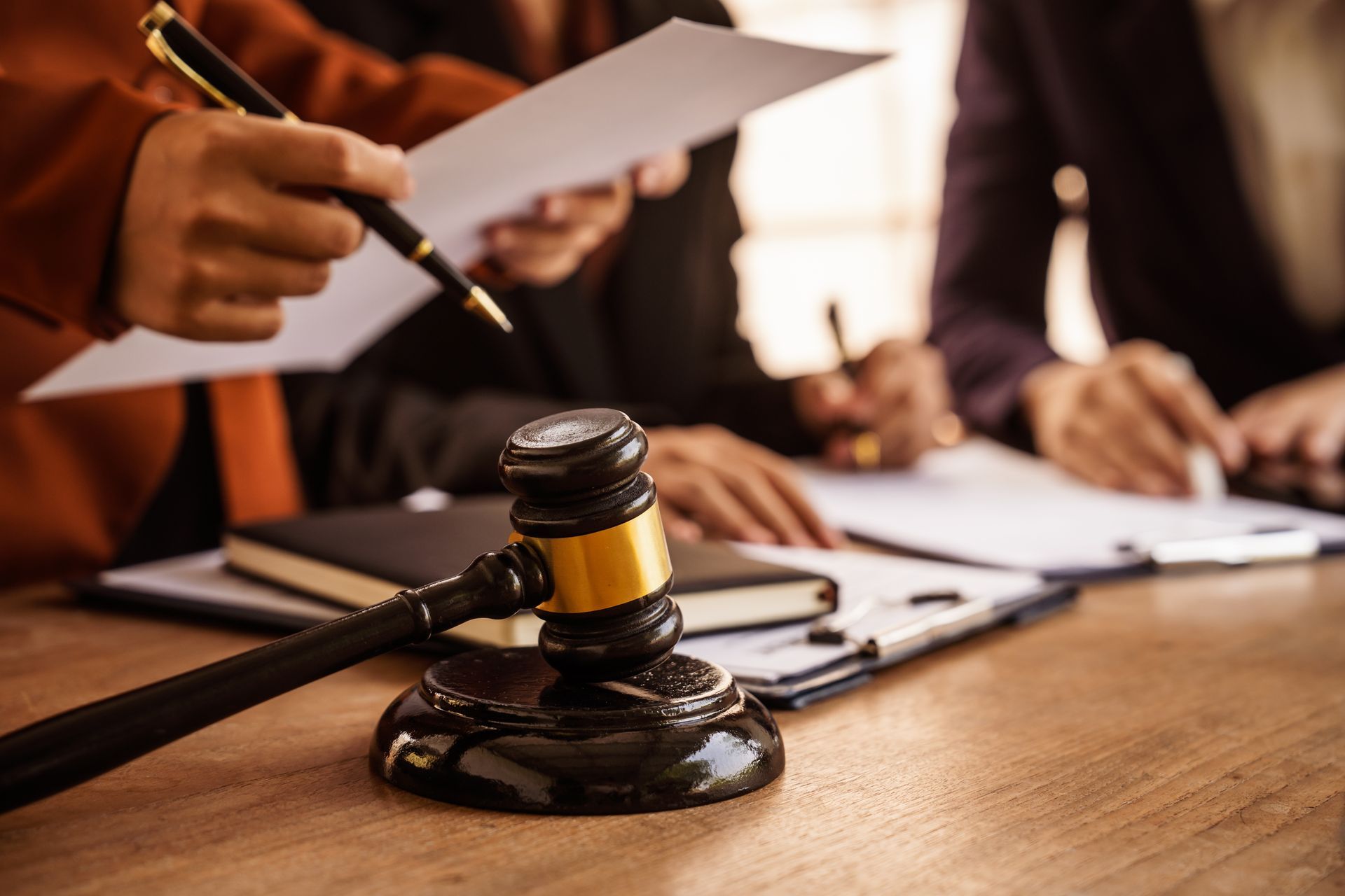 Gavel on a desk as legal professionals review documents during a criminal defense case meeting Gavel on a desk as legal professionals review documents during a criminal defense case meeting