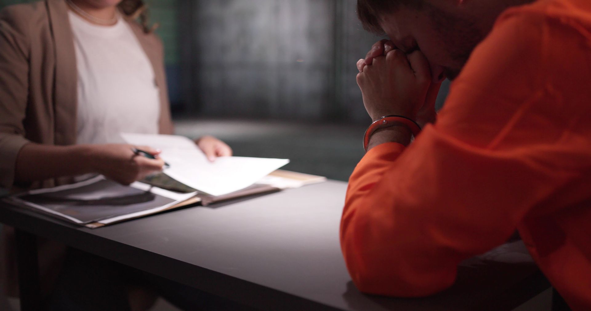 Two people at a table, one holding papers, in a dimly lit room. Two people at a table, one holding papers, in a dimly lit room.