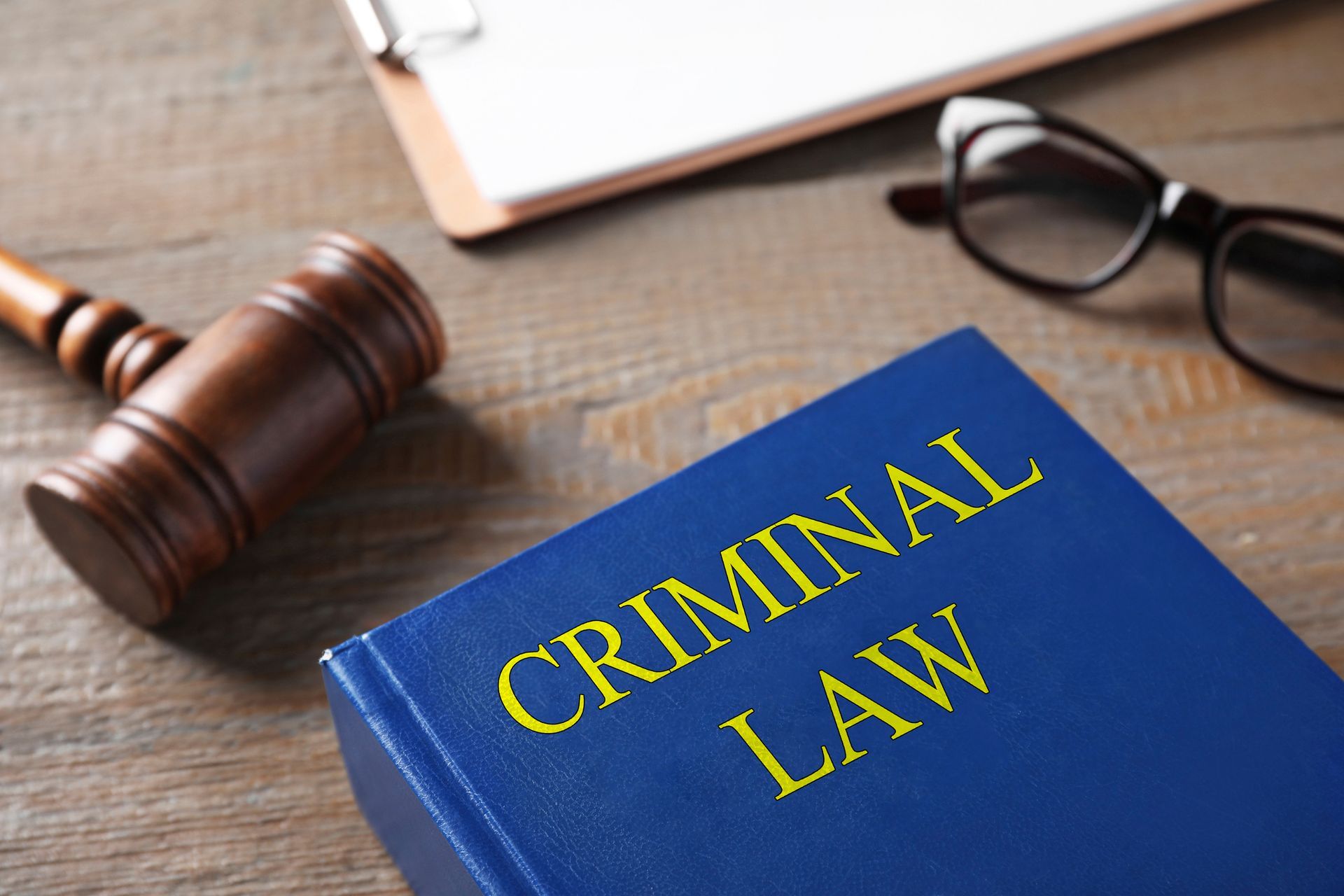 A gavel, a pair of eyeglasses, paperwork, and a criminal law book on a wooden table in Melbourne, FL