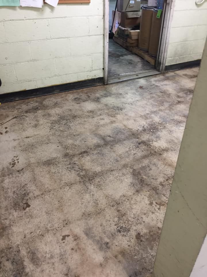 A hallway with worn, light-colored square floor tiles stained with dirt, leading into a room filled with boxes.