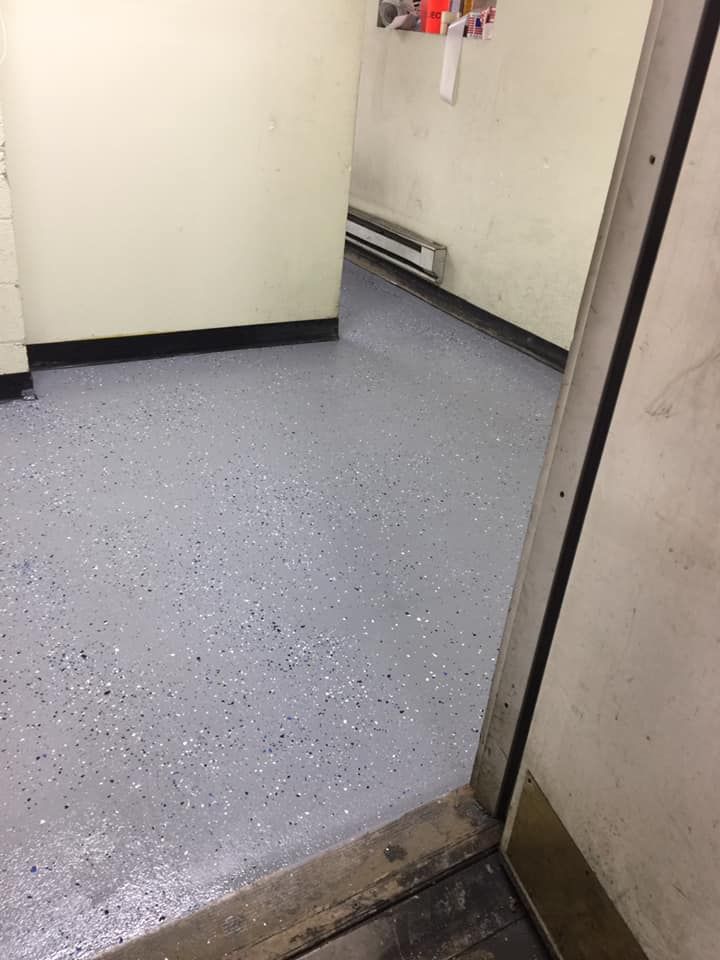 An interior room with a gray speckled epoxy floor and light-colored walls, viewed from a doorway.