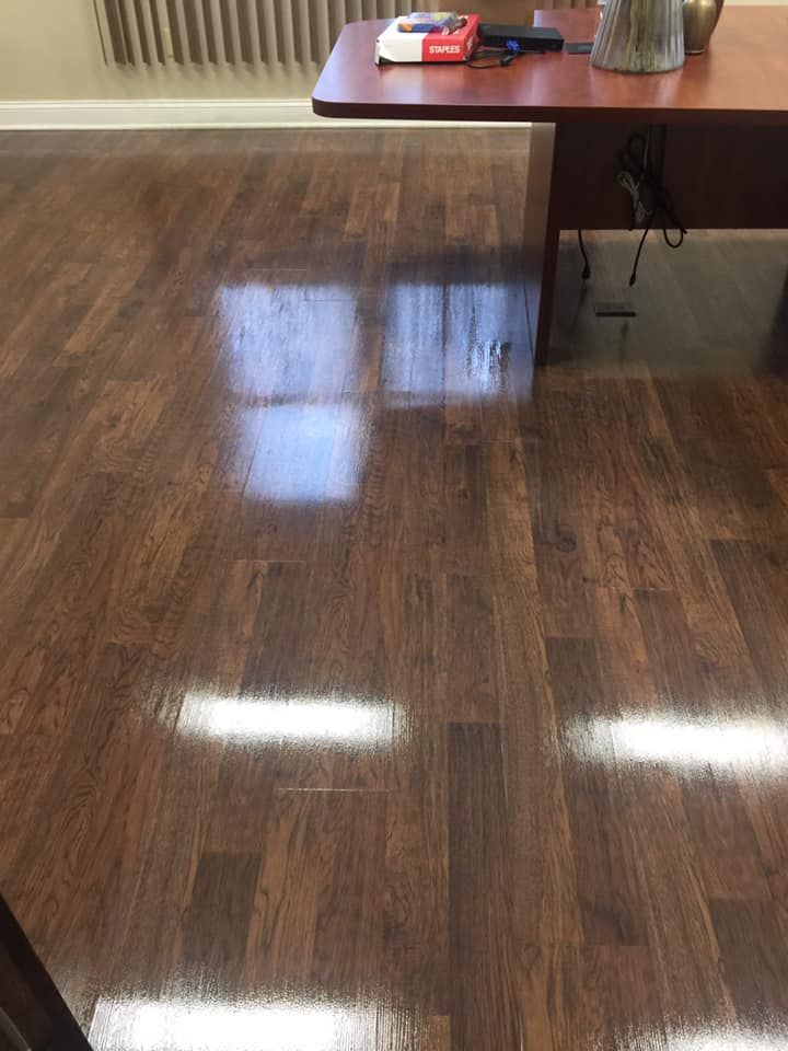 A high-angle view of a polished dark brown wood floor reflecting indoor lighting beneath an office desk.