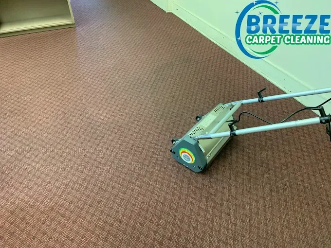 A professional carpet cleaning machine sitting on a patterned reddish-brown carpet in an office space.