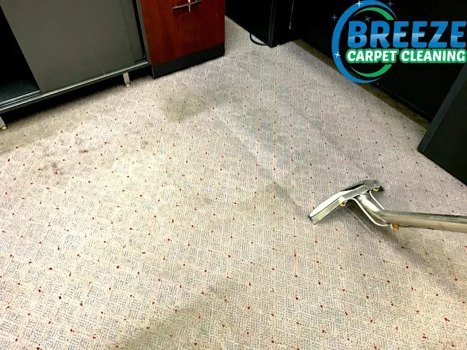 A metal cleaning wand performs a deep clean on a spotted, light-colored patterned carpet in an office space.