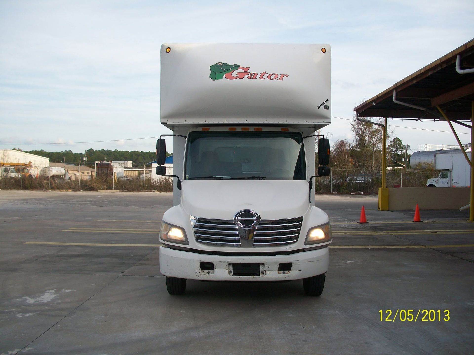 White delivery truck parked in an open lot under a cloudy sky, front view.