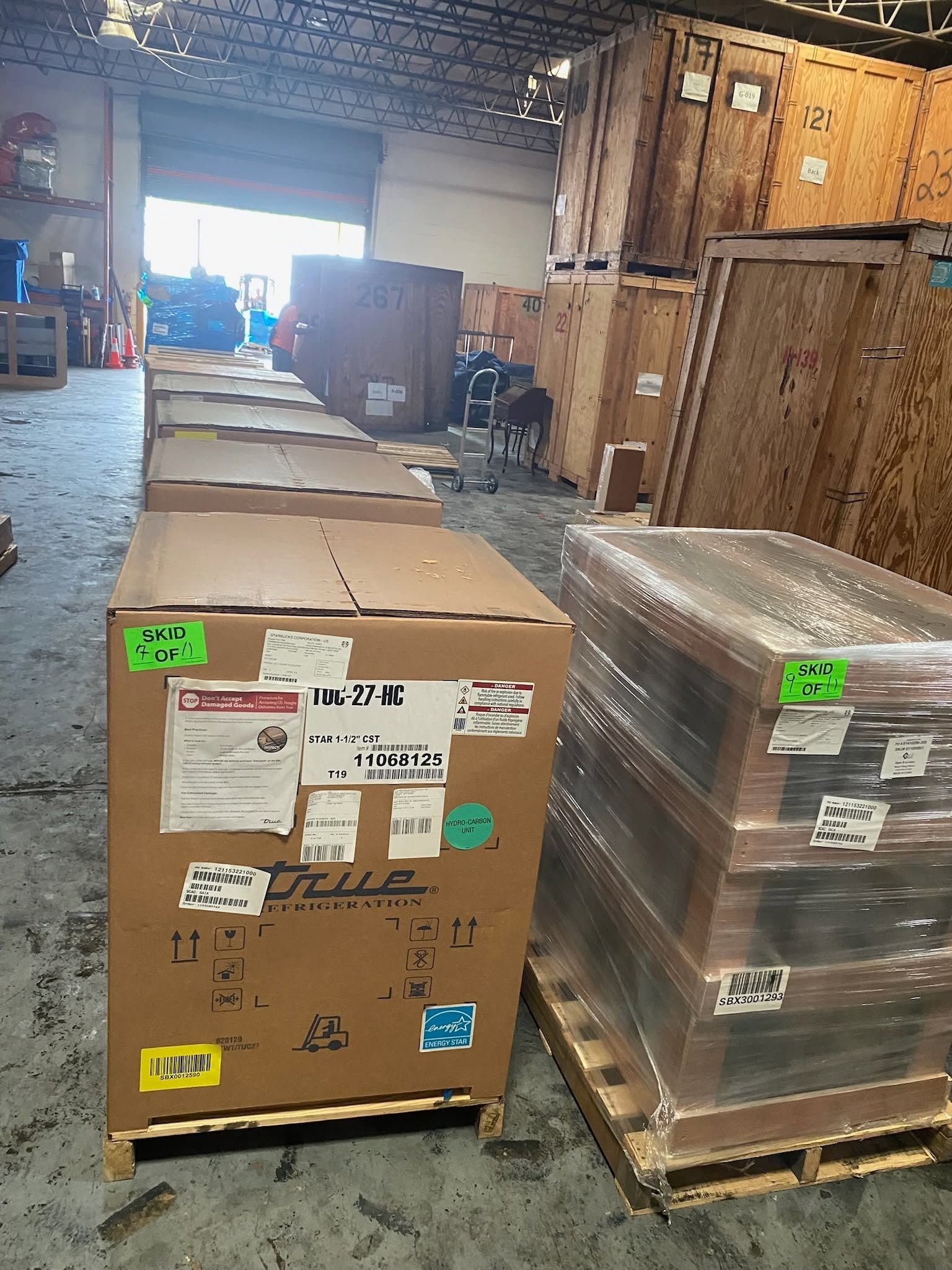 Warehouse with two shrink-wrapped pallets of boxed goods on wooden pallets near a loading area.