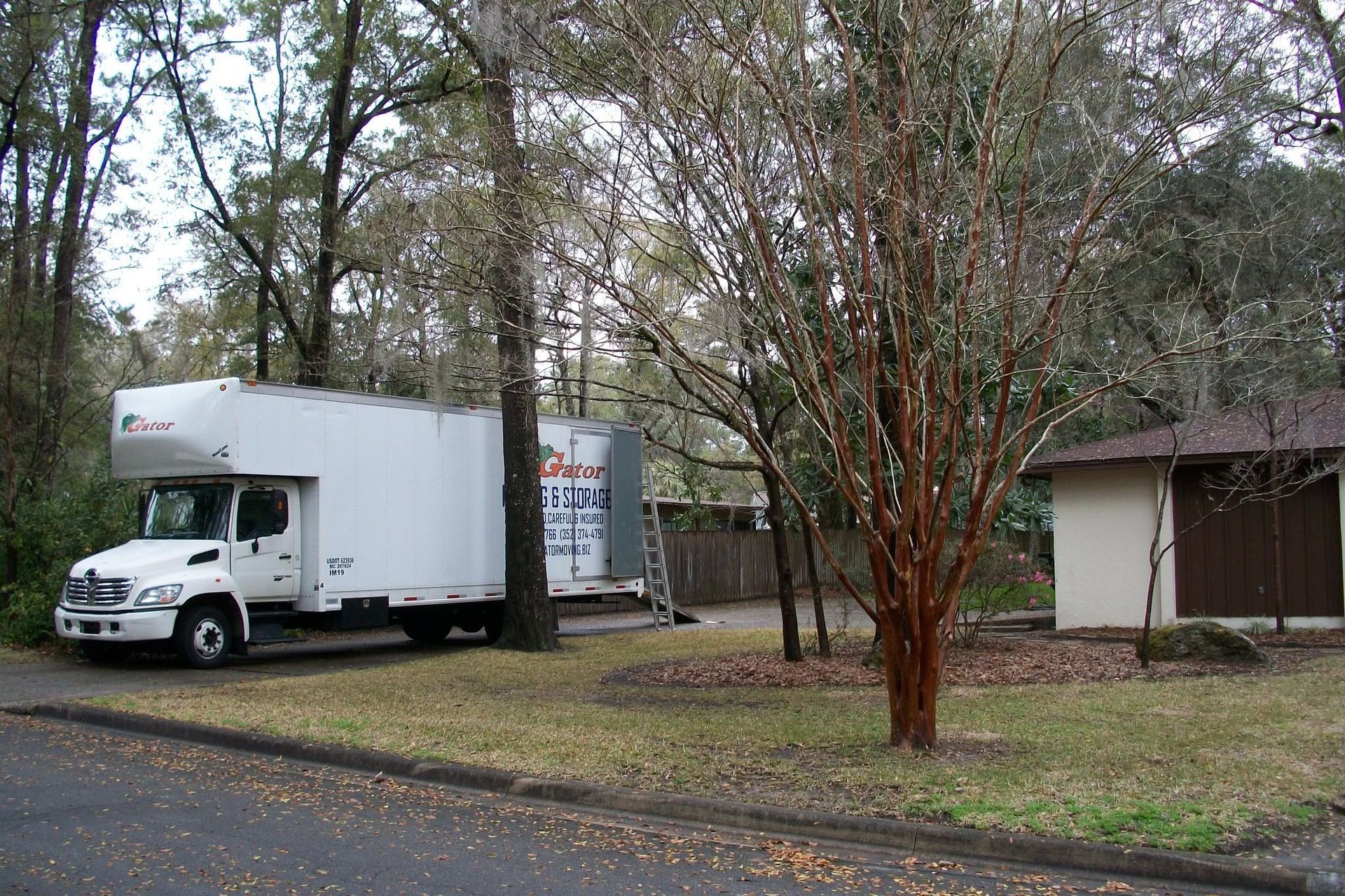 White box truck parked by a small building in a wooded lot on a cloudy day