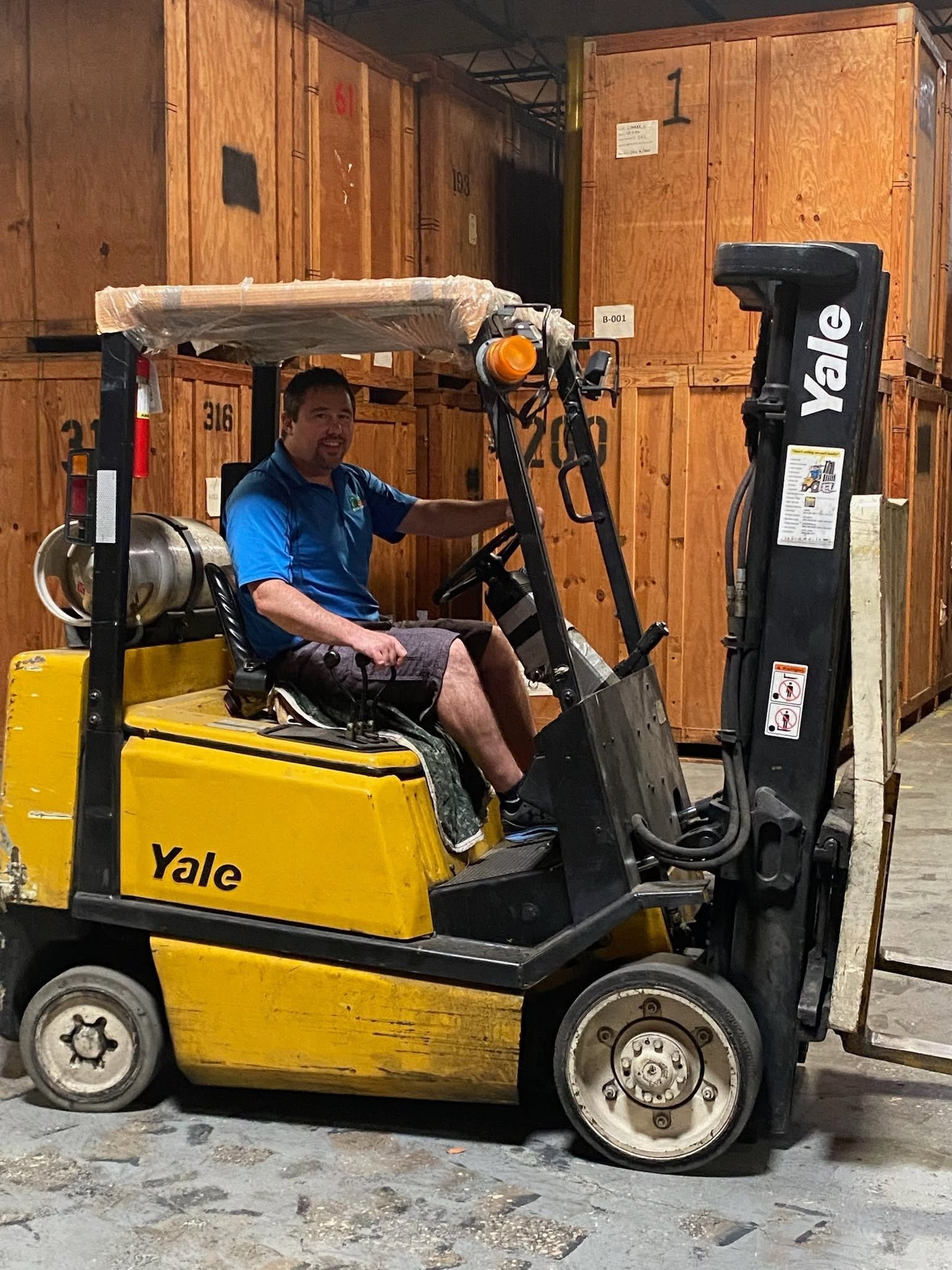 Yellow Yale forklift with a driver inside, parked in a wooden warehouse.