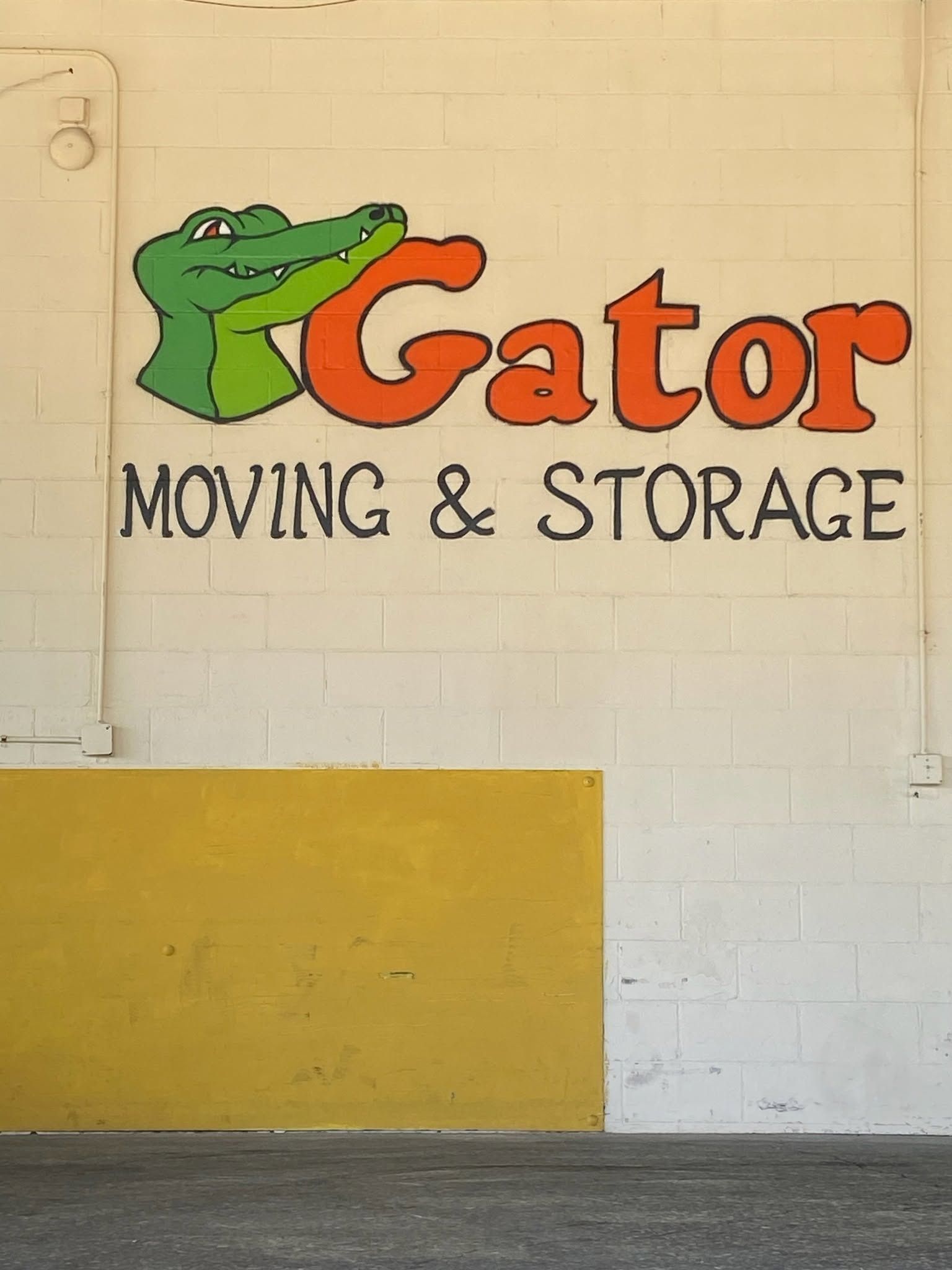 Gator Moving & Storage sign with green alligator logo on a white and yellow wall
