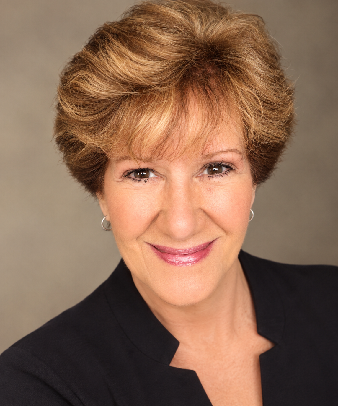 Smiling person with curly hair and green sweater, standing with arms crossed against a light gray background