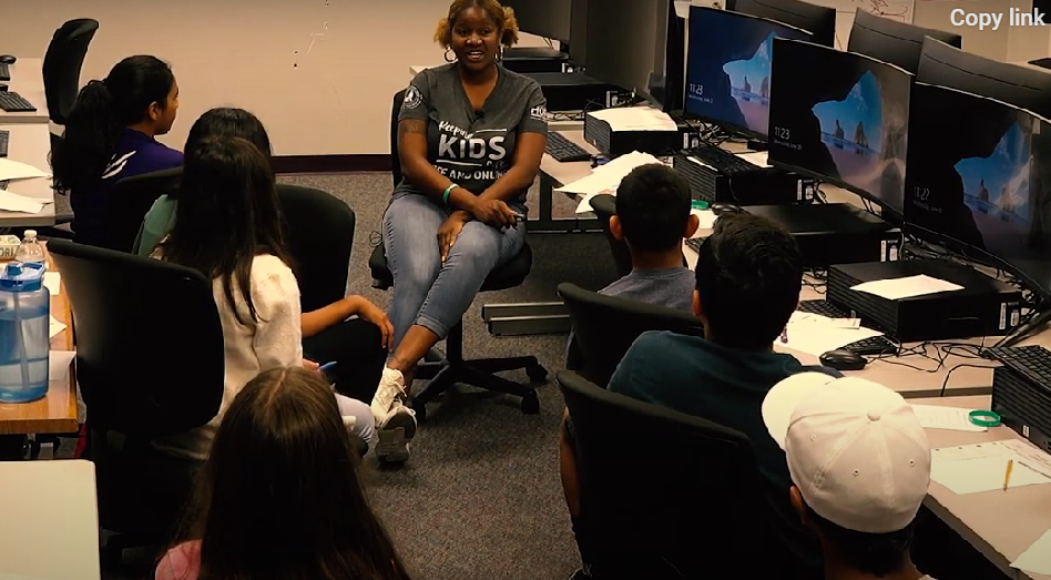 Students seated in a computer lab while an instructor speaks at the front.