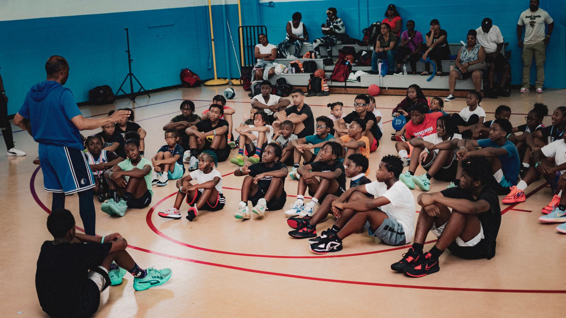 Basketball coach instructing a seated group of students in a gymnasium