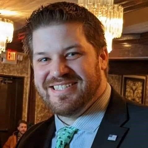 Smiling man in a suit and green tie standing indoors under chandeliers
