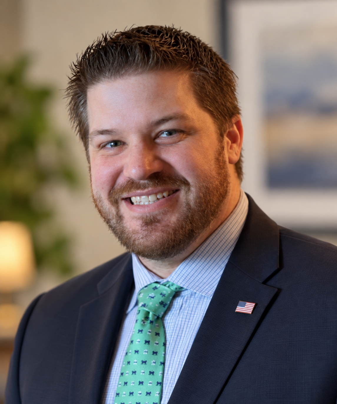 Smiling man in a suit and green tie standing indoors under chandeliers