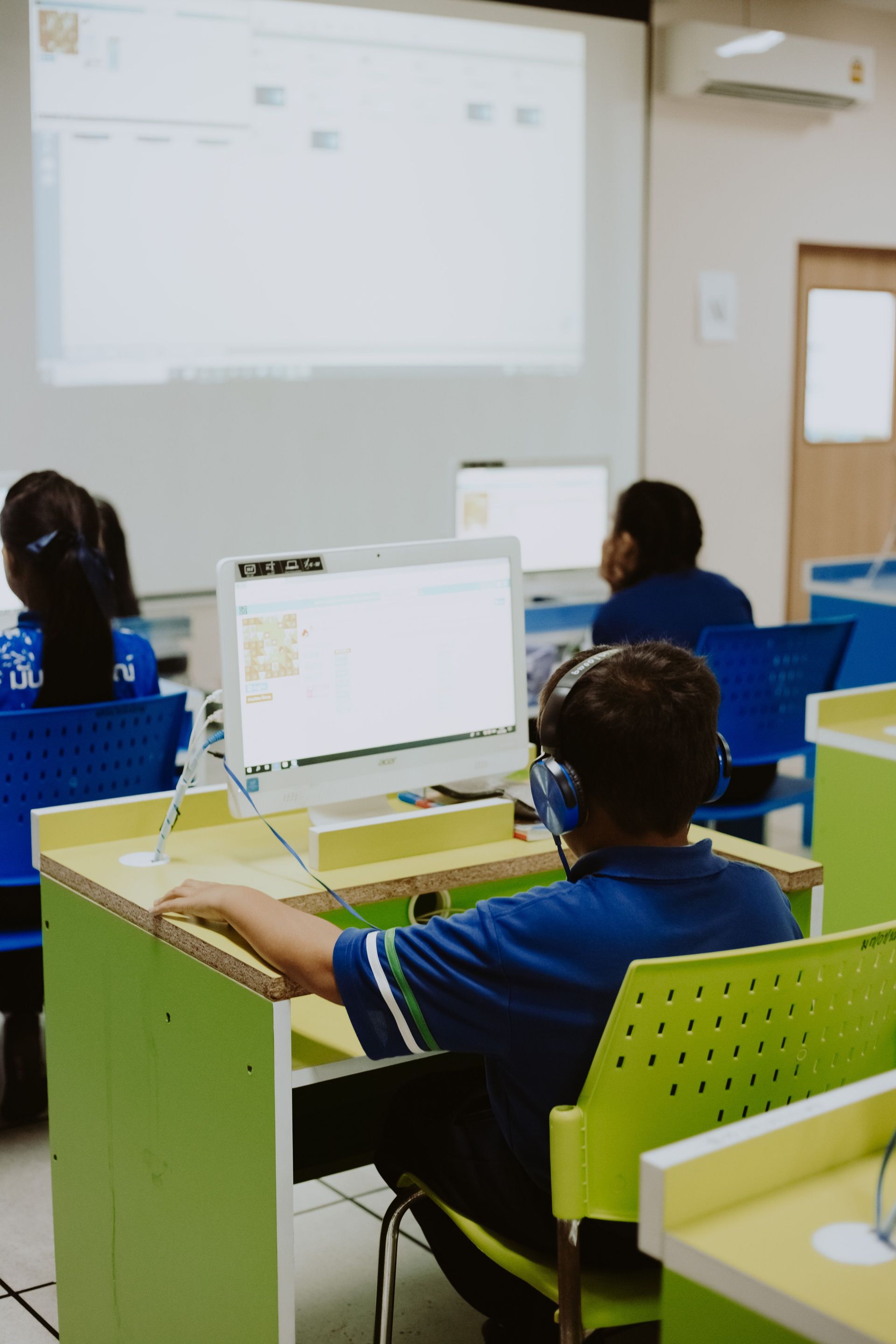 Students seated at computers in a classroom facing a projected screen