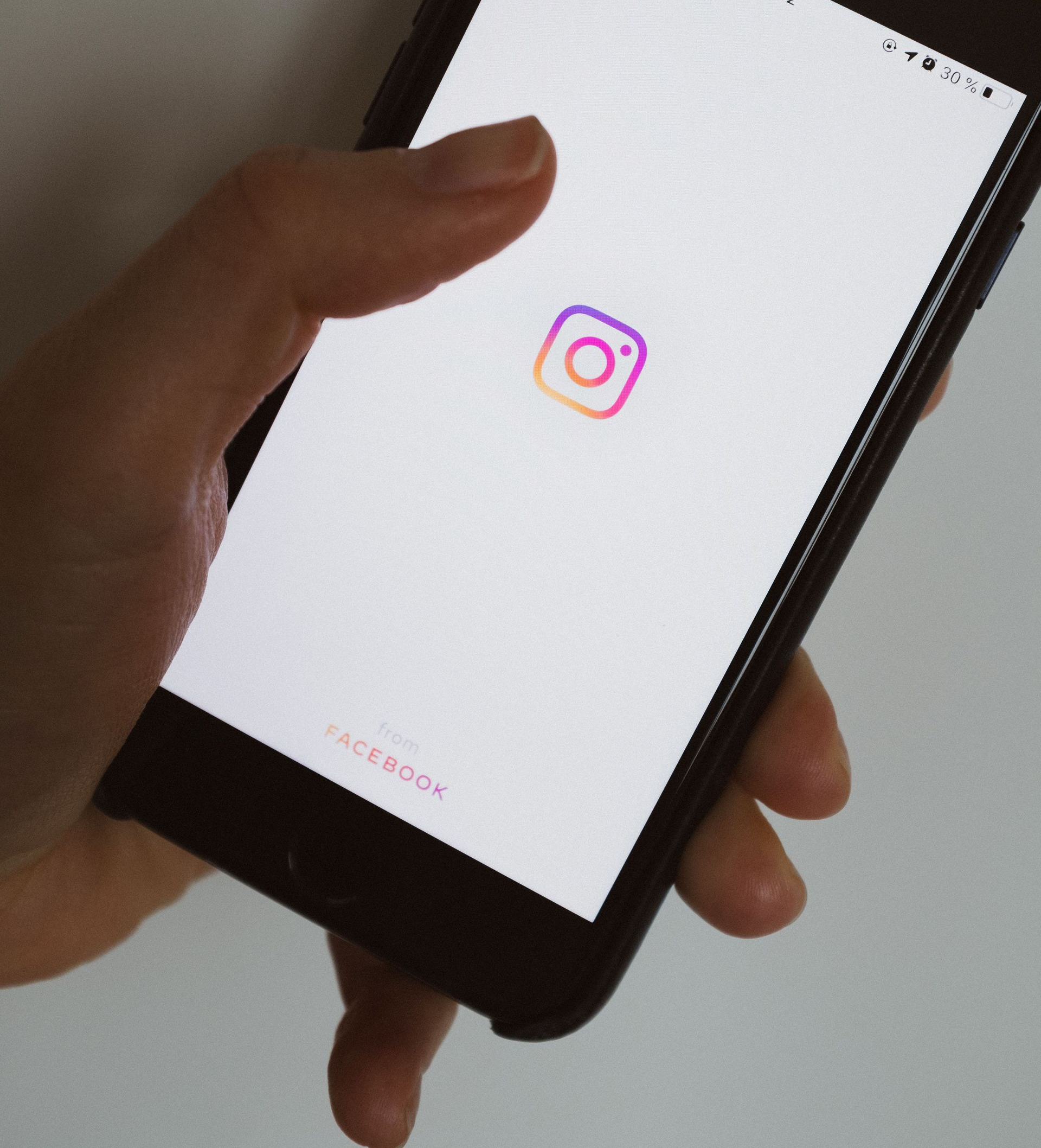 Hand holding a smartphone displaying the Instagram app logo on a white screen