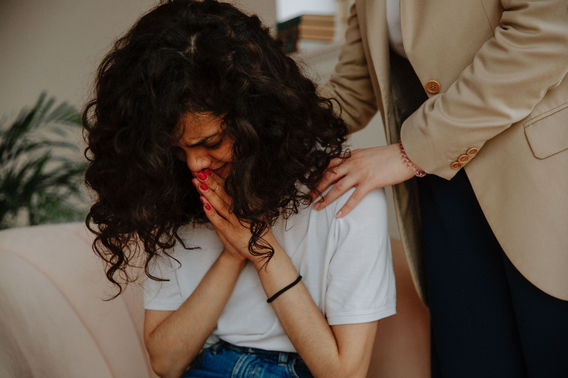 Distressed woman crying while another person comforts her with a hand on her shoulder