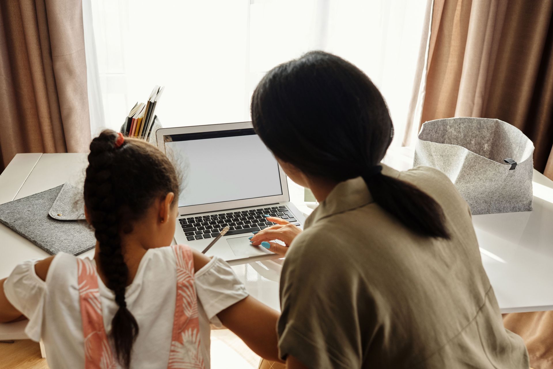 Two people sit at a table using a laptop beside a window with curtains and a tissue box
