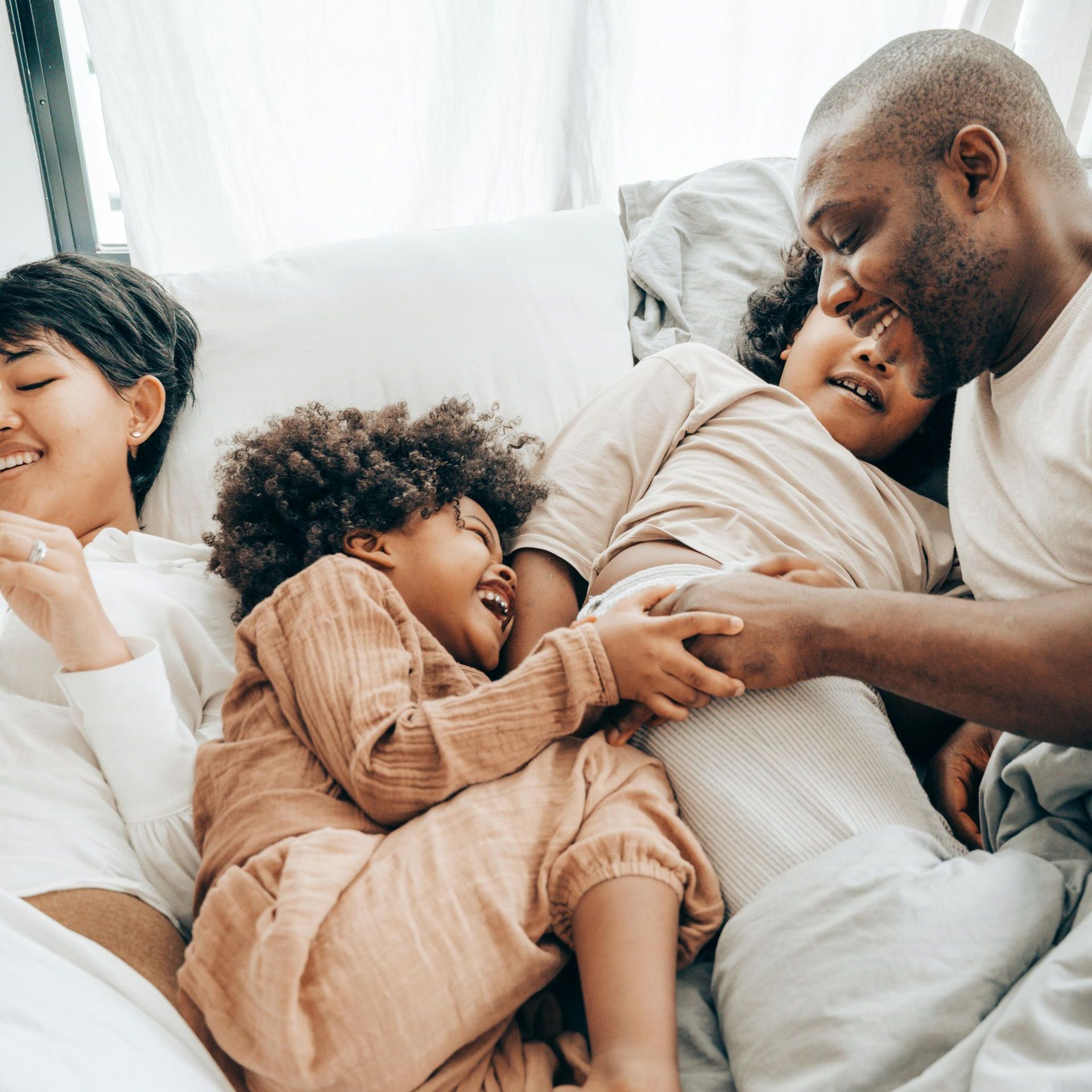 A family is laying in bed together and playing with each other.