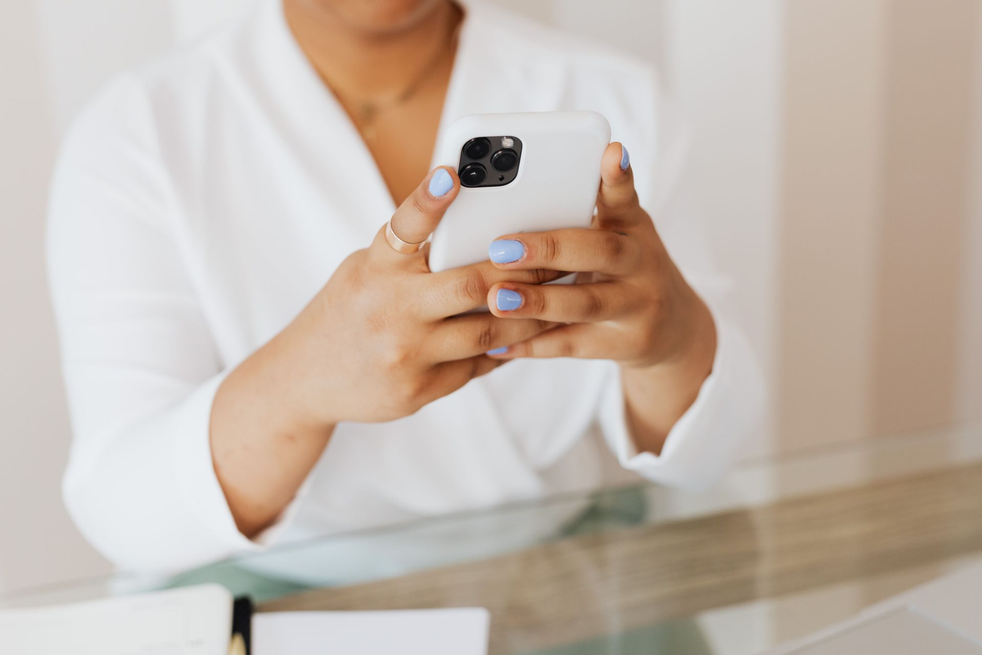 Person holding a smartphone at a table, wearing a white shirt