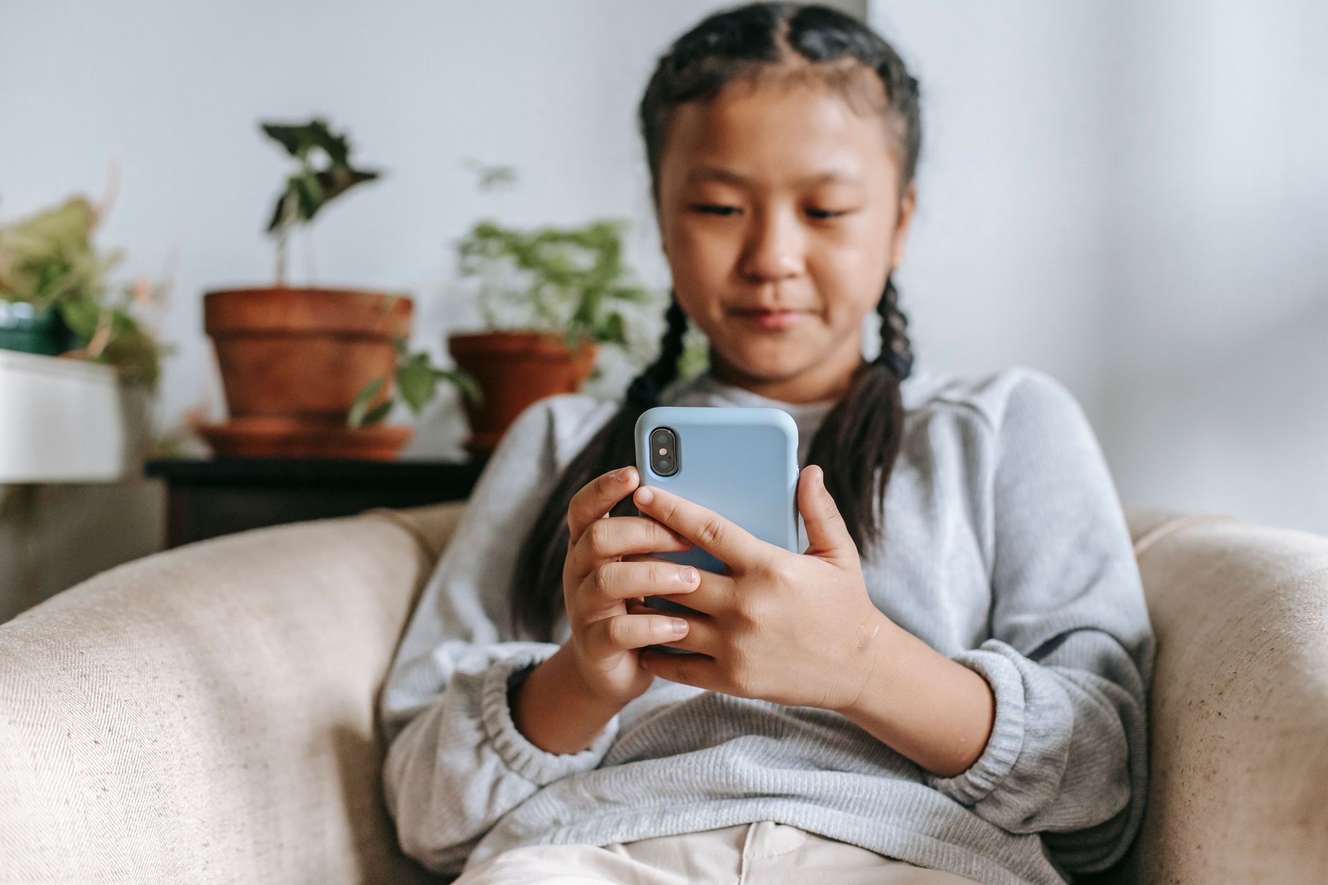 Person sitting on a couch and looking at a smartphone, with potted plants in the background