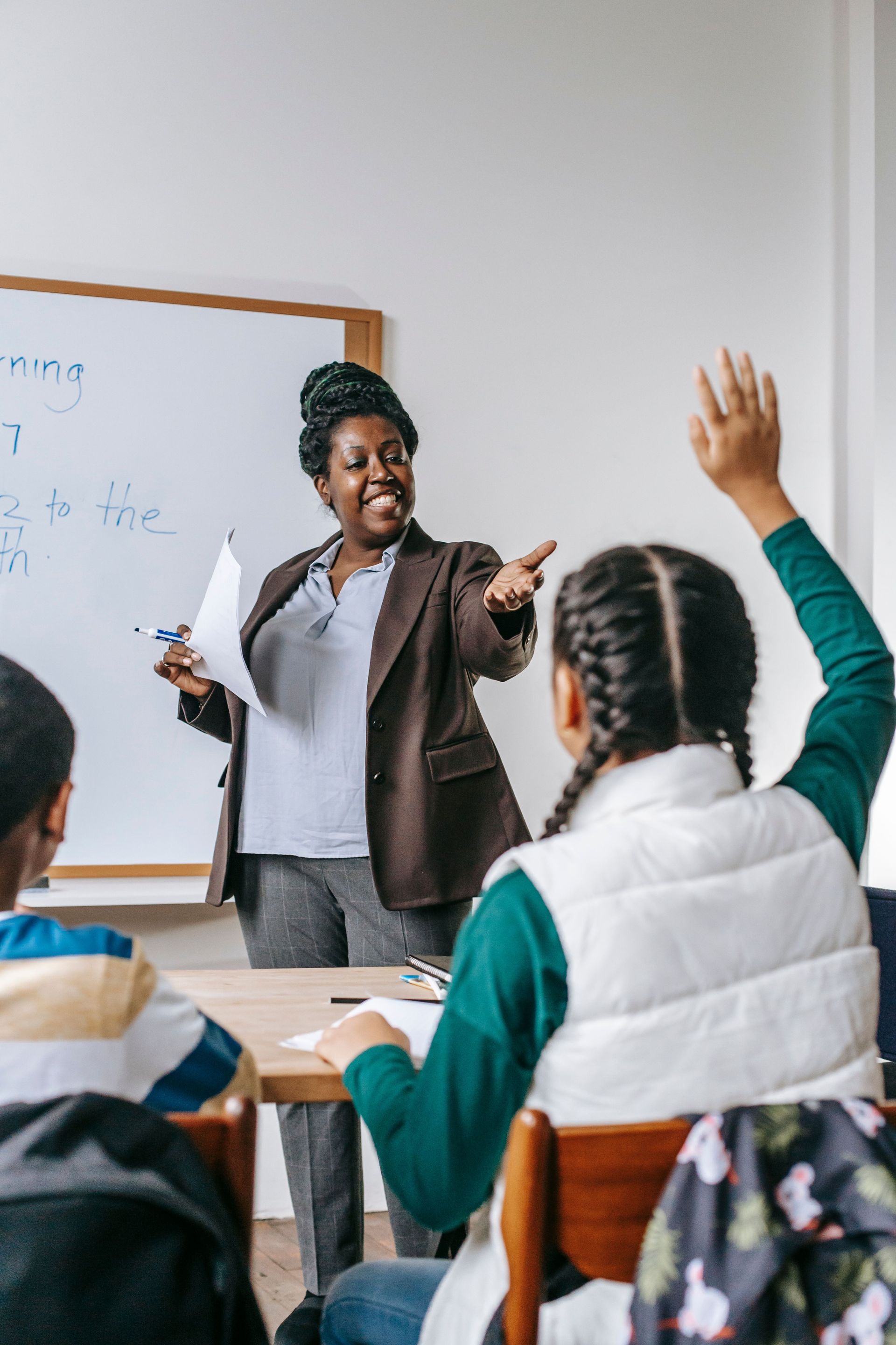 Teacher pointing at students in a classroom as one raises a hand