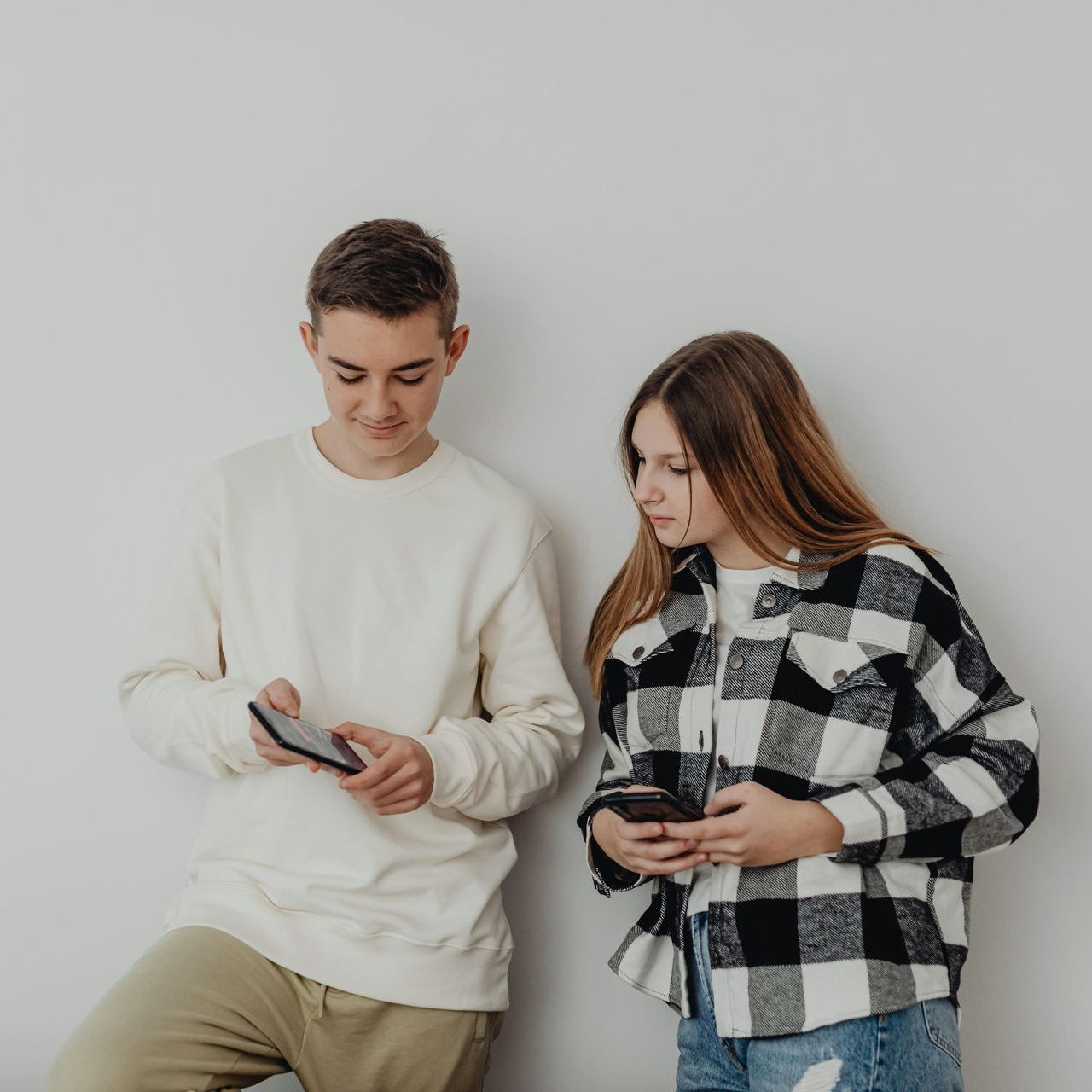 A man and a woman are standing next to each other looking at their phones.