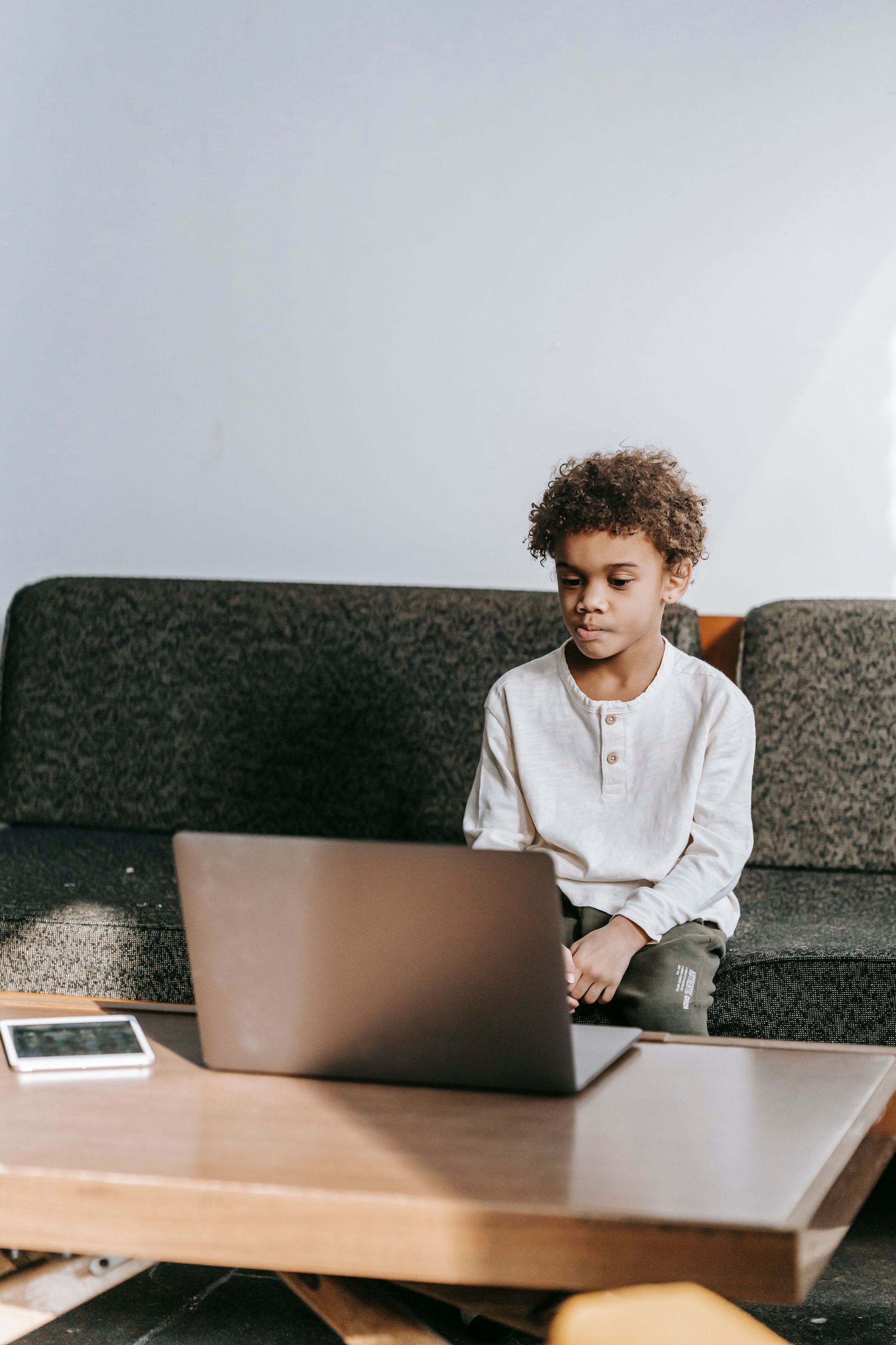 Kid sitting on a couch using a laptop at a coffee table in a bright living room.